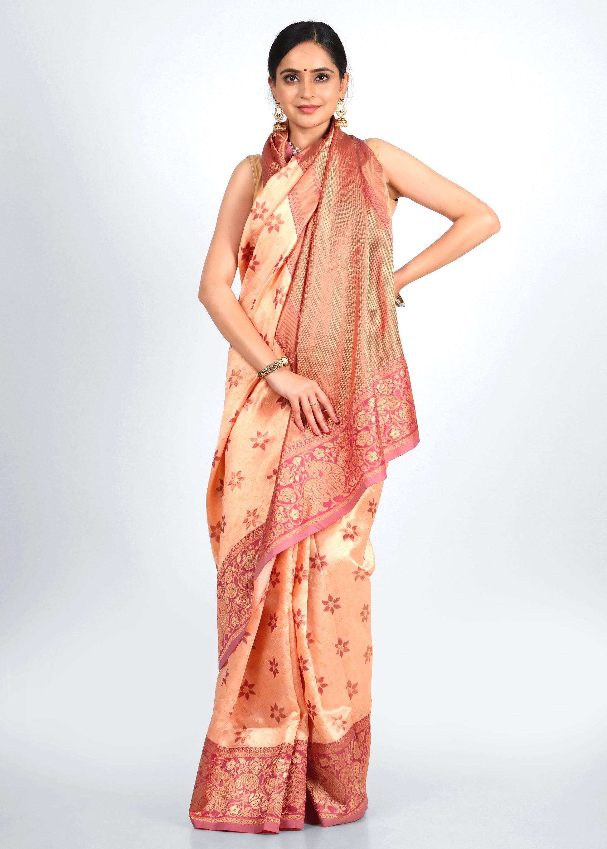 Woman in an elegant peach and gold silk saree with intricate floral patterns, adorned with golden jewelry.