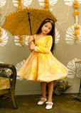 "Adorable girl wearing a vibrant yellow floral dress holding a decorative umbrella, perfect for festive occasions."