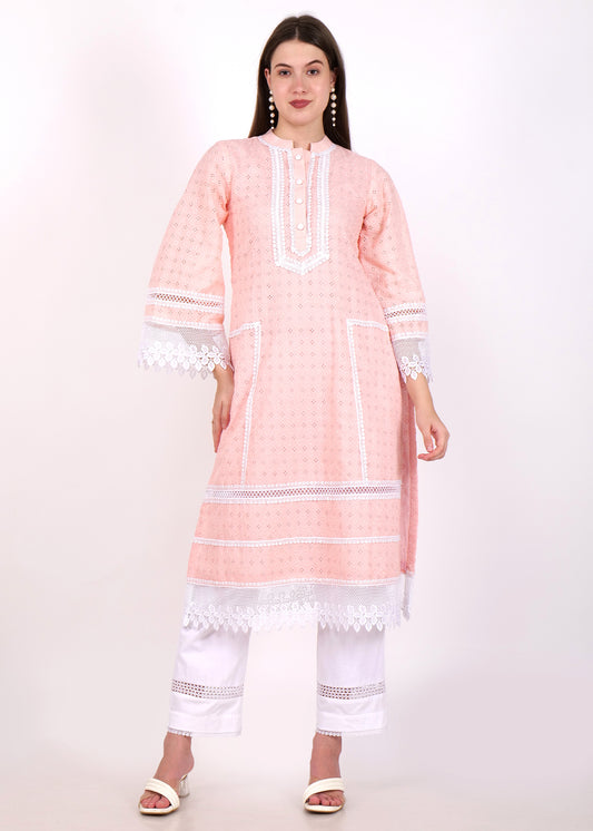 Woman wearing a pastel pink embroidered kurta with white lace details, front view, paired with white pants and pearl earrings