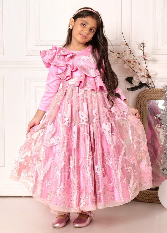 Young girl wearing a pink ruffled gown with floral lace details, posing against a soft, white backdrop.