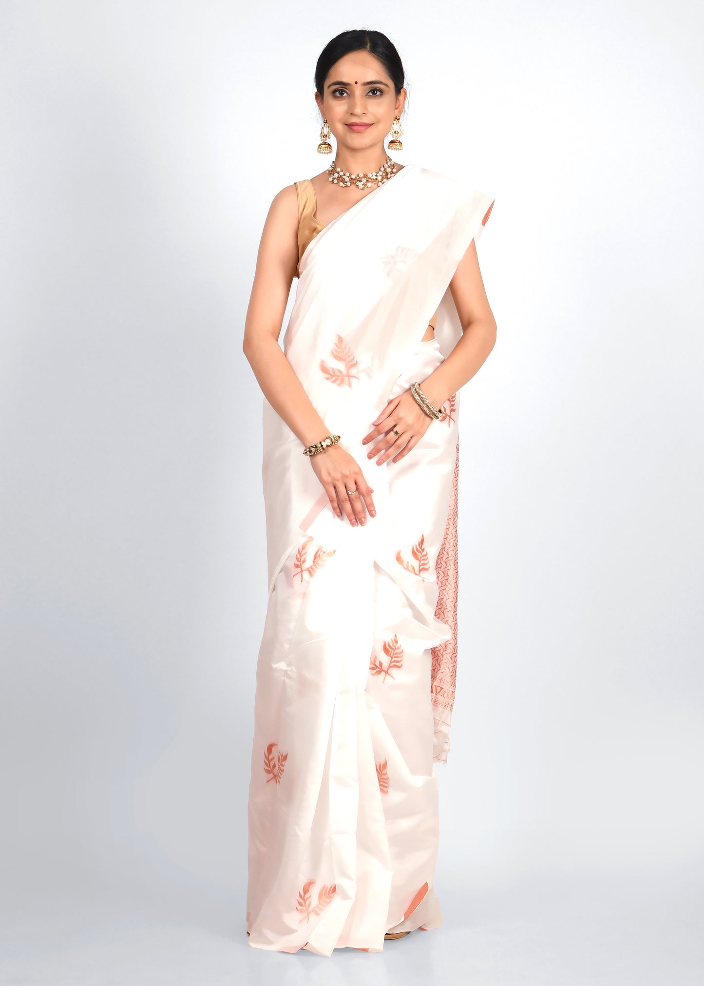 Model in a white handwoven silk saree with soft orange floral motifs and delicate borders, showcasing a timeless traditional look