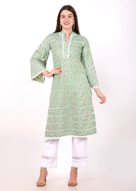 Woman wearing a green floral print kurta with intricate lace details and white pants, standing confidently in heels