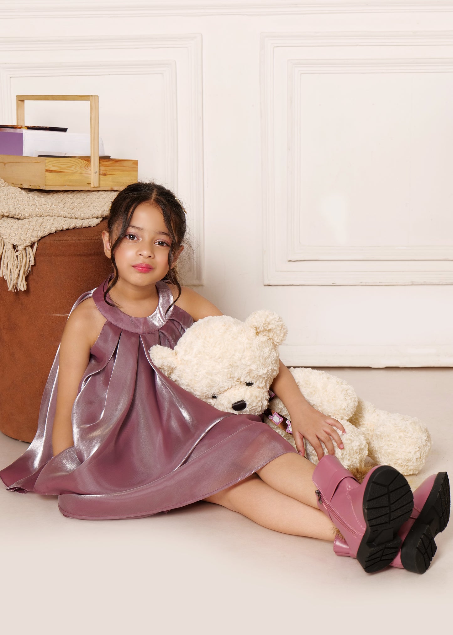 Young girl sitting with a teddy bear, wearing a stylish sleeveless purple satin dress and matching pink boots, perfect for special occasions