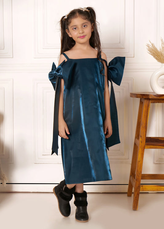 Little girl wearing a teal satin dress with oversized bows on the sleeves, standing confidently in front of a minimalist background.