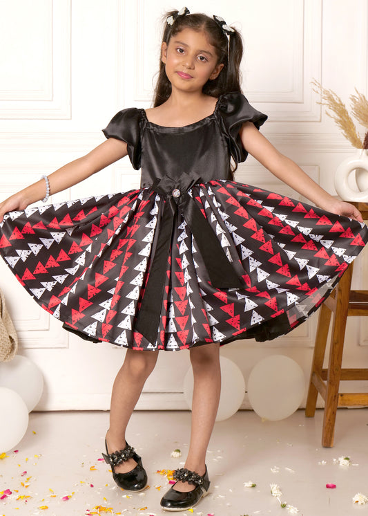 Girl in a black and red geometric triangle dress with puff sleeves, holding the sides of her dress, styled for a kids' fashion shoot