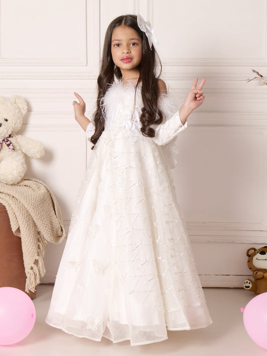 Young girl in a beautiful white butterfly-embellished gown with sequin details and feather accents, posing in a dreamy setting with a teddy bear.