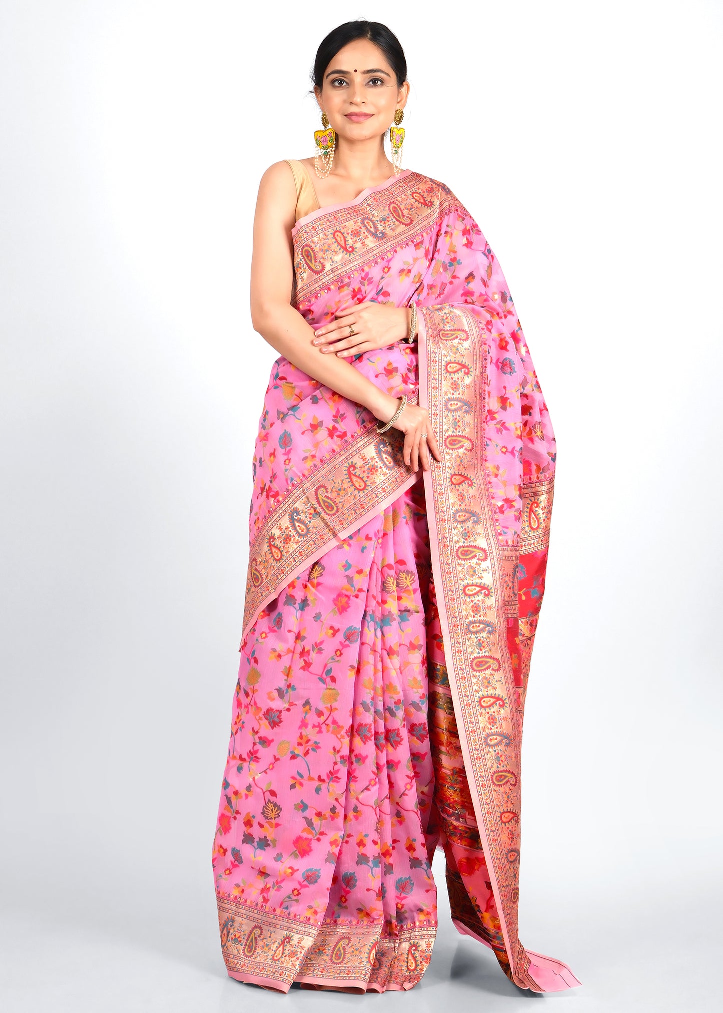 Woman in a pink floral saree with intricate golden borders, standing in a poised traditional pose