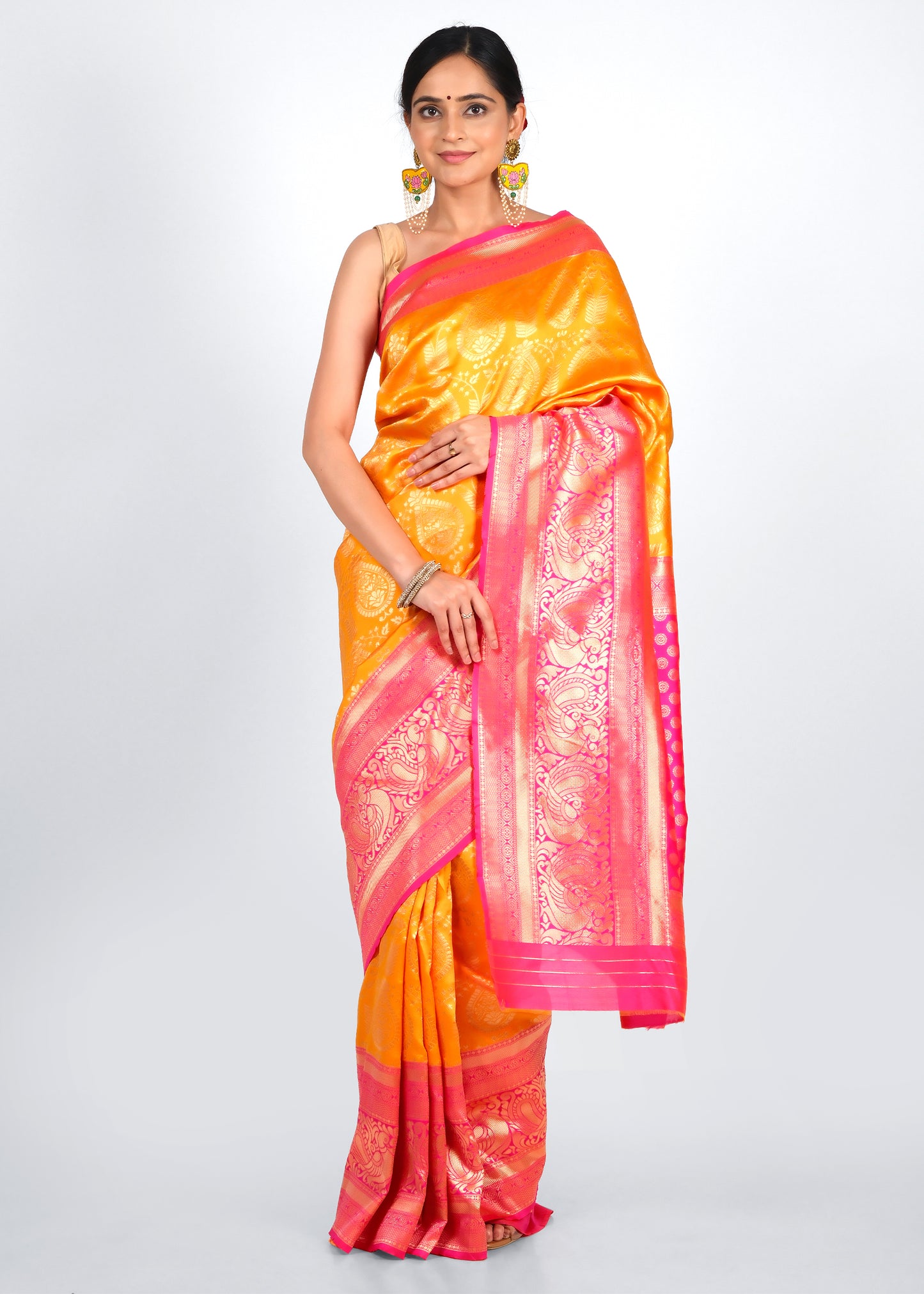 Woman dressed in a vibrant orange and pink silk saree with intricate golden motifs, exuding a traditional and festive charm