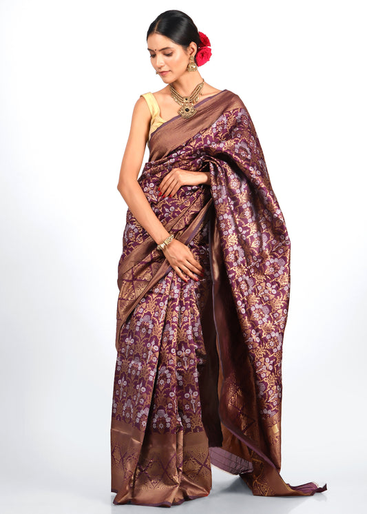 A woman wearing an elegant maroon and gold silk saree with intricate floral patterns and traditional Indian jewelry, posing gracefully in a classic Indian outfit.