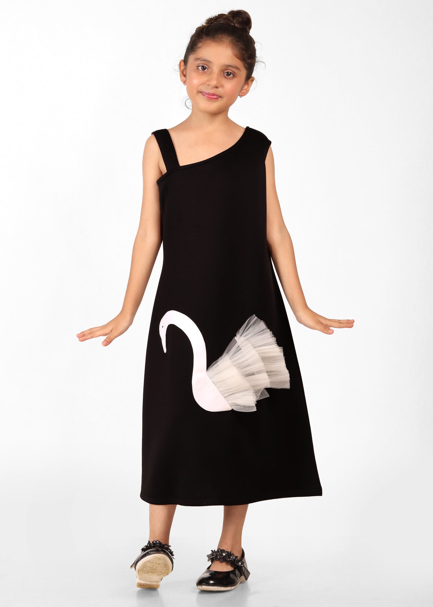 Little girl in an elegant black one-shoulder dress featuring a stylish white swan applique and layered tulle skirt, posing confidently for a fashion photoshoot