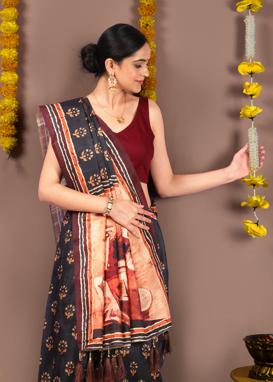 Model wearing a traditional black saree with intricate floral designs and tassel border, styled with maroon blouse and gold jewelry