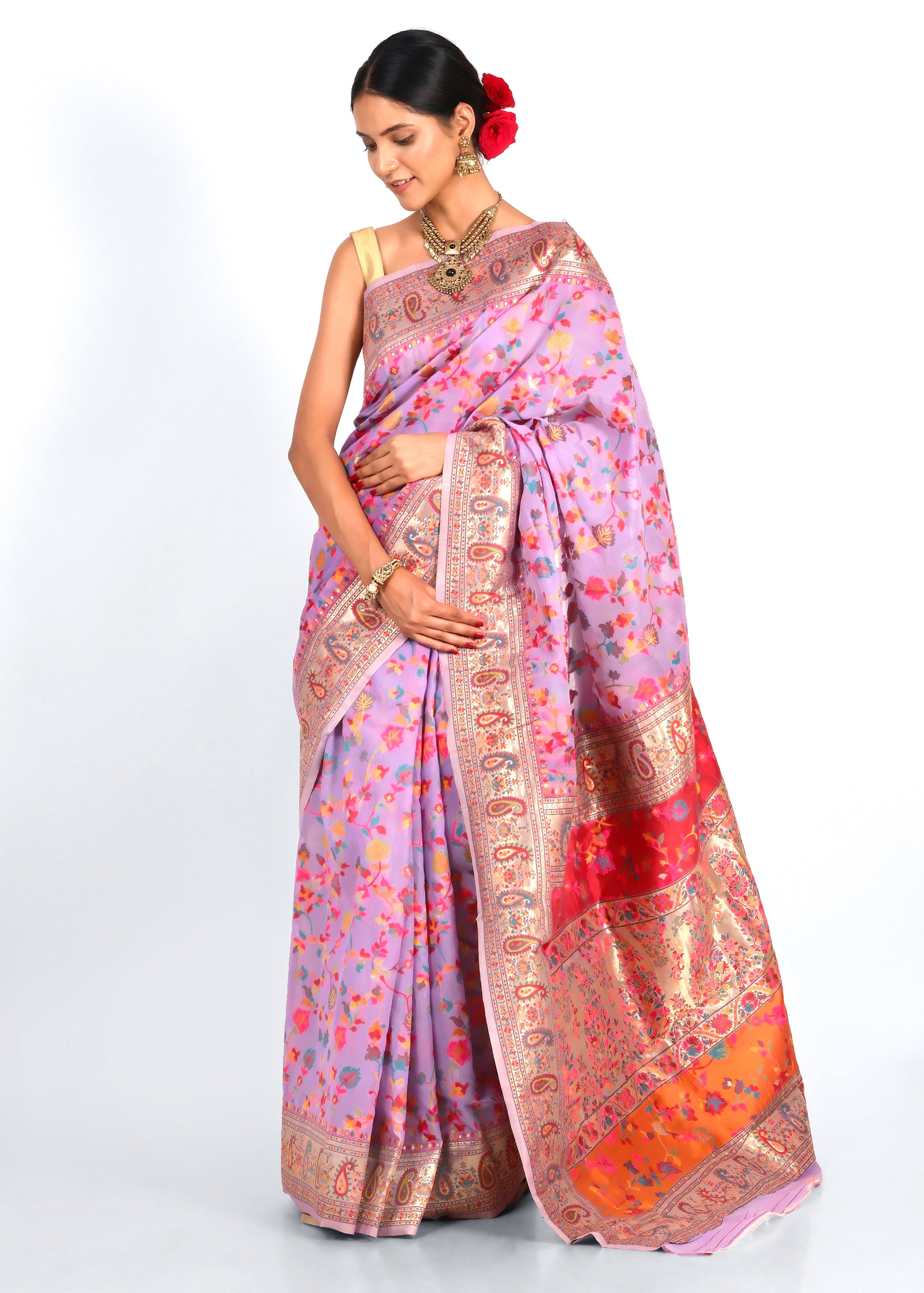 Woman in elegant lavender and floral print saree with intricate gold paisley border, draped gracefully while showcasing traditional jewelry and floral hair accessory