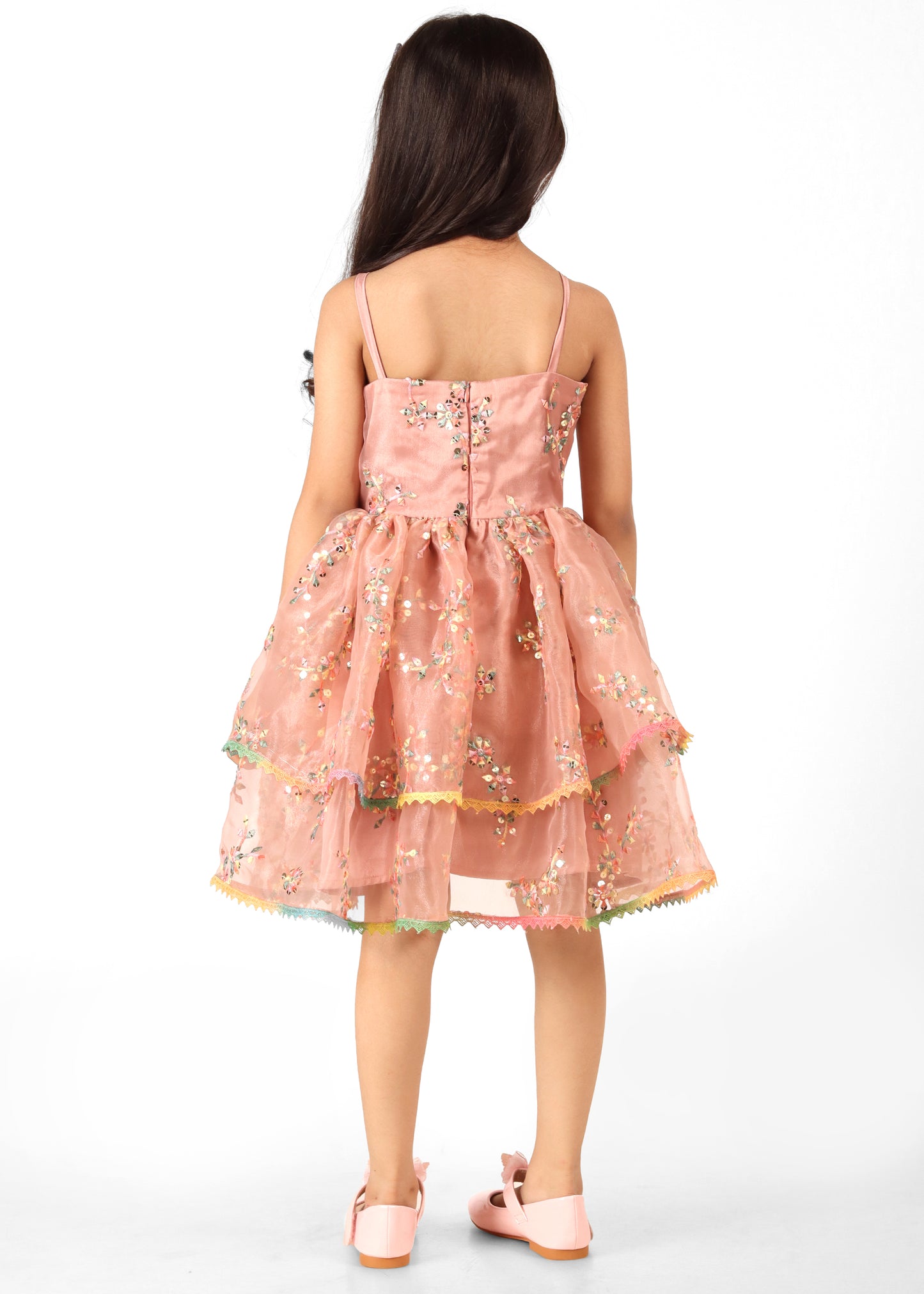 Back view of a young girl wearing a peach floral dress with spaghetti straps and sequin detailing, featuring a full skirt.