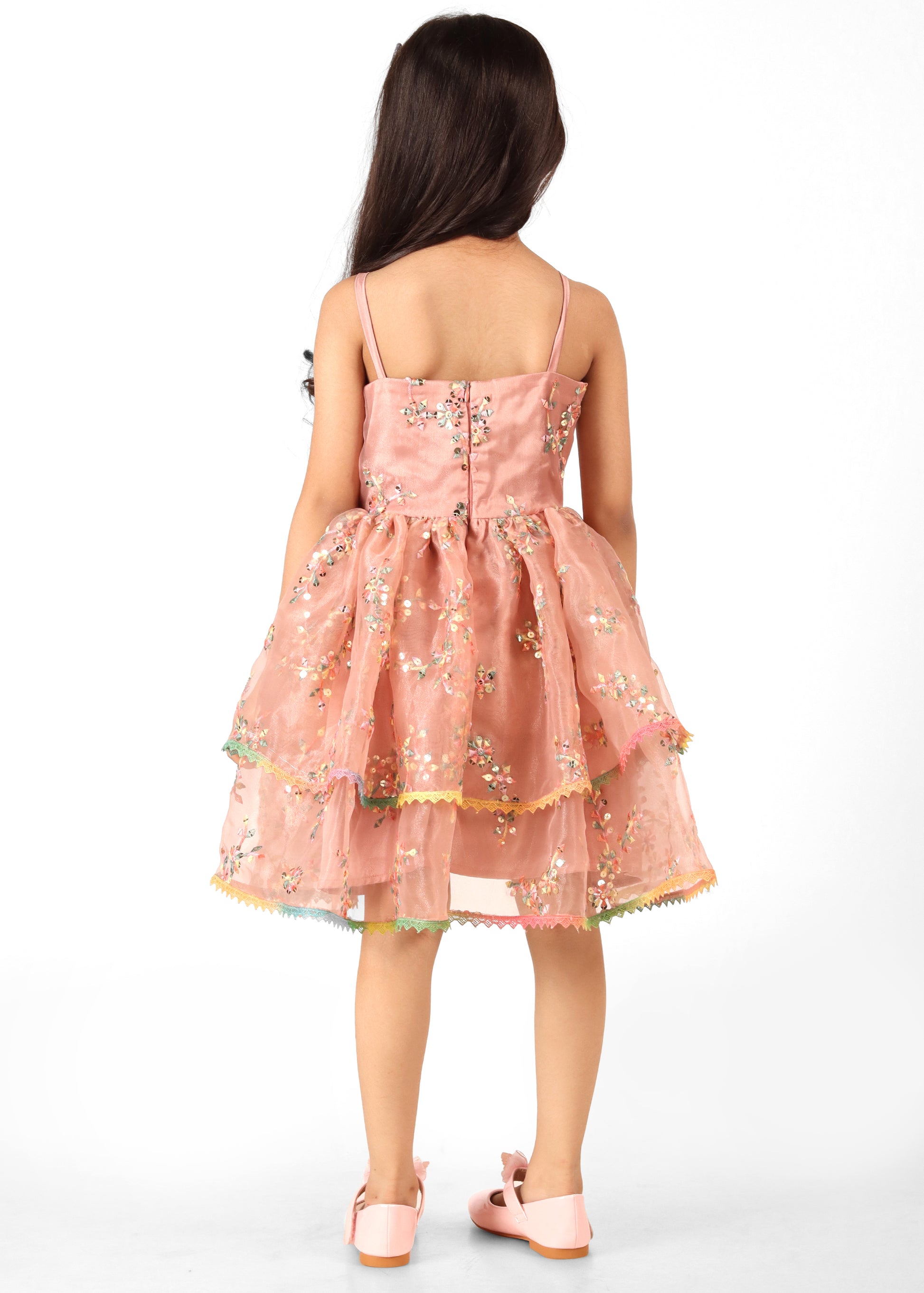 Back view of a young girl wearing a peach floral dress with spaghetti straps and sequin detailing, featuring a full skirt.