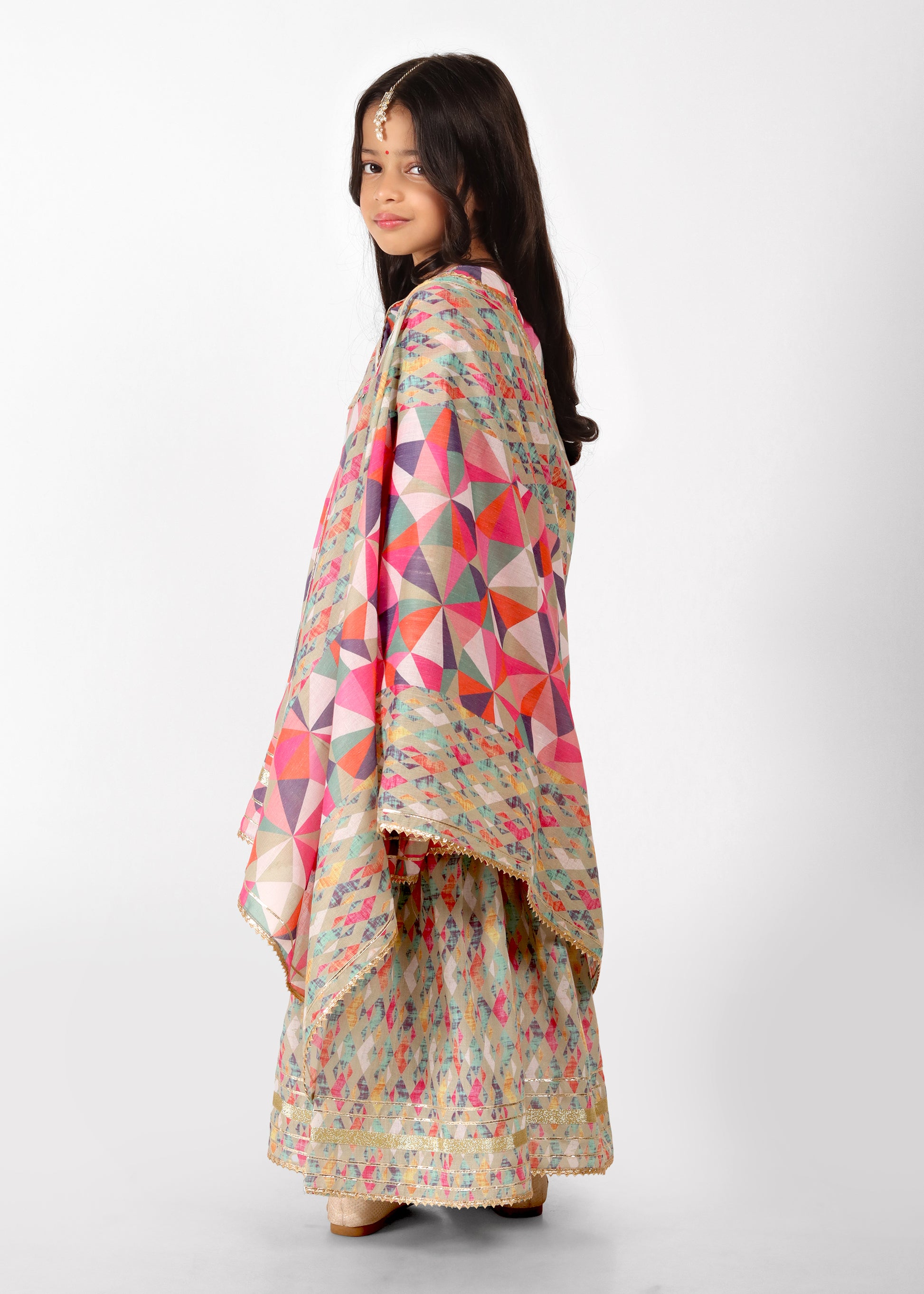 Side view of a young girl wearing a colorful geometric patterned kurta with a matching dupatta and palazzo. The ethnic outfit is ideal for festivals and showcases intricate designs and vibrant colors.