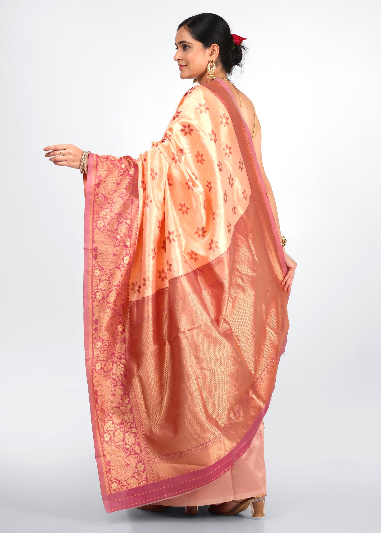 Rear view of a woman in a peach silk saree with a rich gold pallu, showcasing floral patterns and traditional weaves.