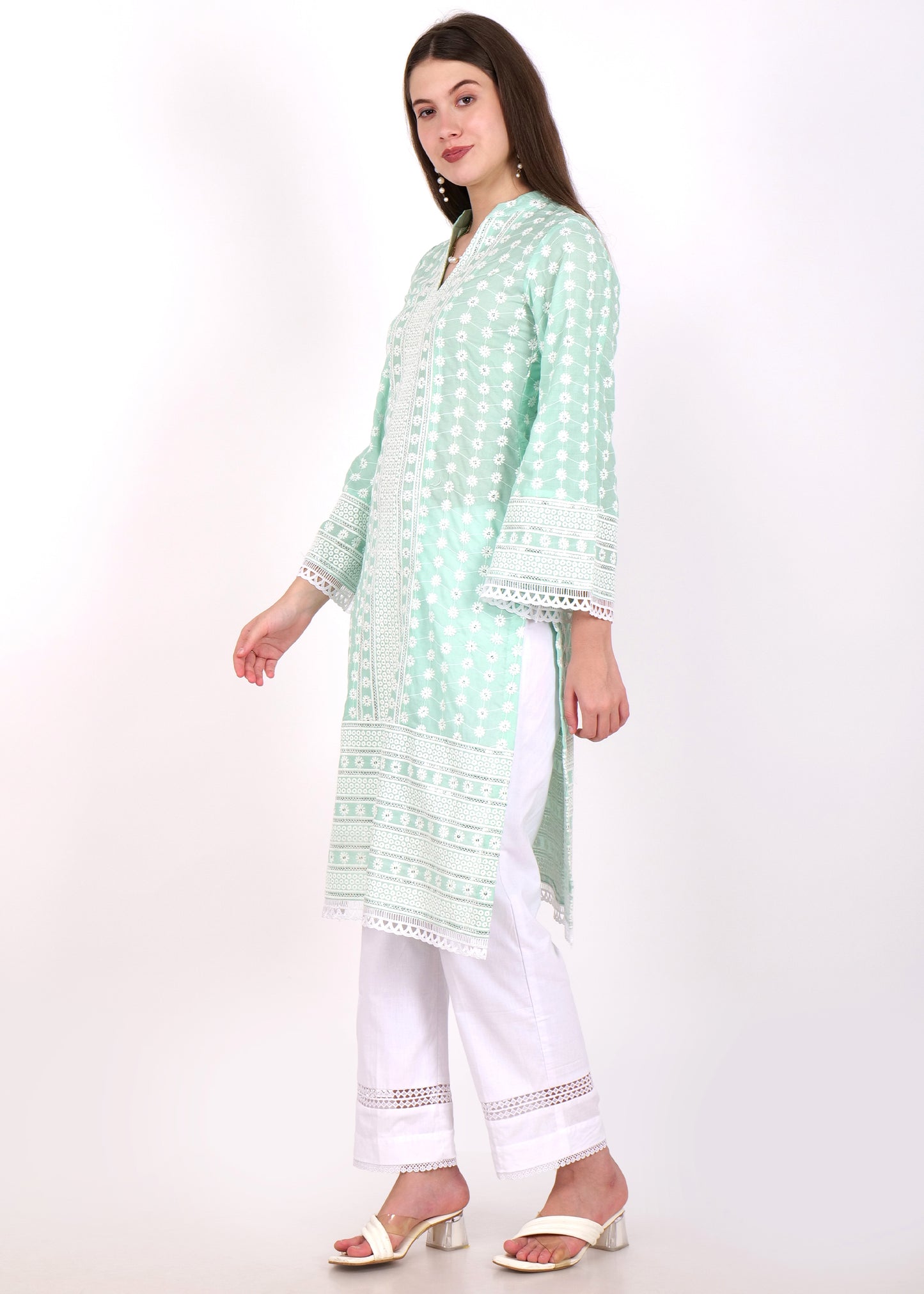 Side profile of a woman dressed in a pink embroidered kurta with flared sleeves and white lacework, paired with white pants and white sandals