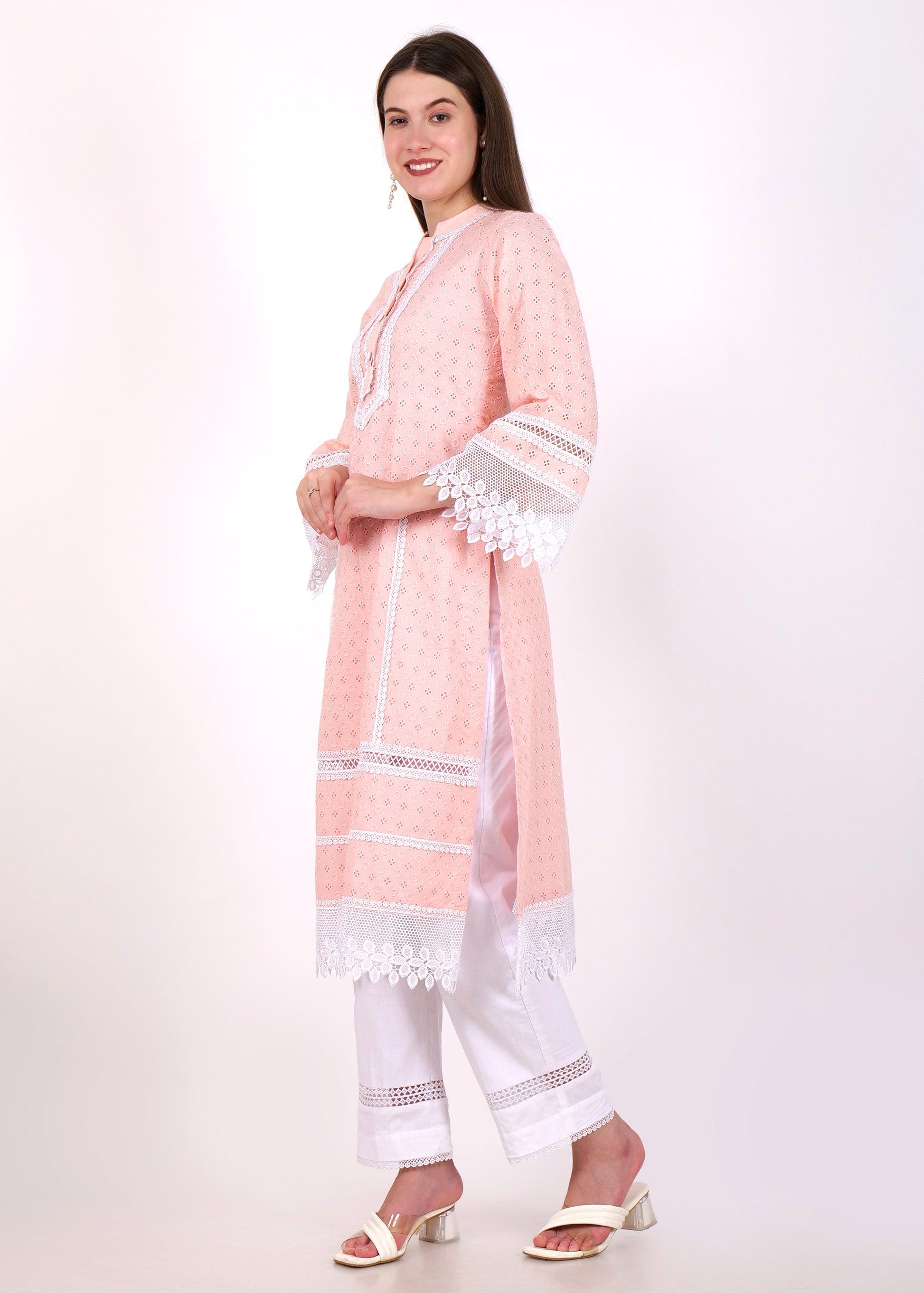 Side view of a woman in a pastel pink kurta with lace trim sleeves and white pants, styled with white heels