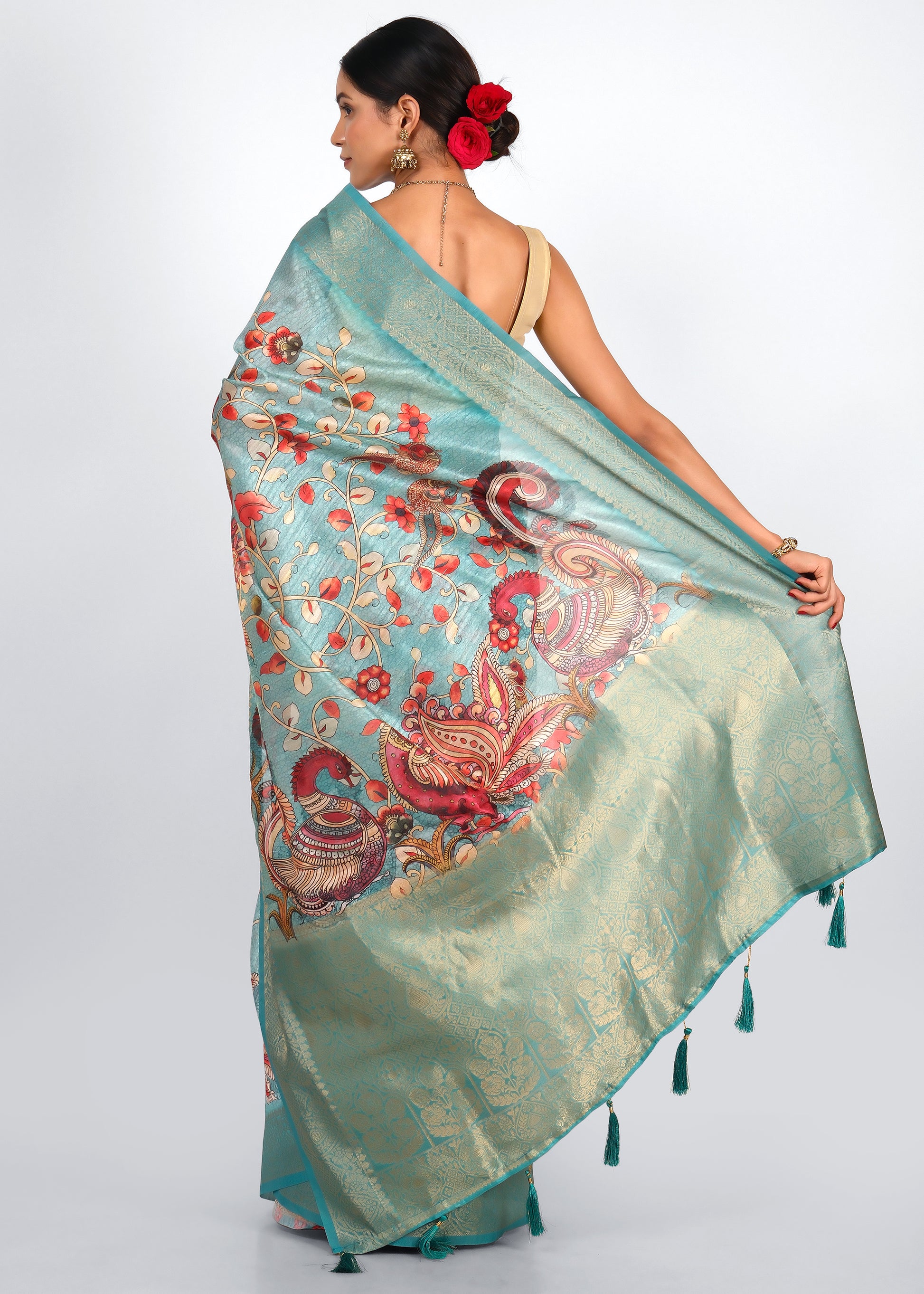 Rear view of a teal saree with vibrant floral and peacock designs on the pallu, highlighting the intricate detailing of the traditional Indian attire