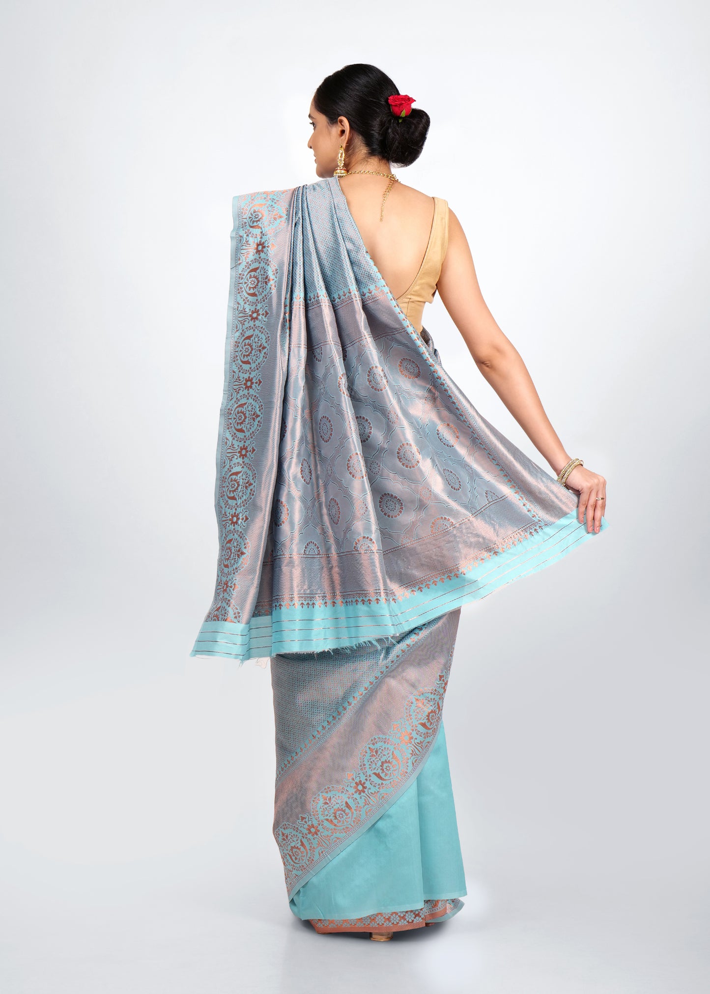 Model wearing a light blue Banarasi silk saree with intricate floral brocade and zari border, accessorized with gold jewelry