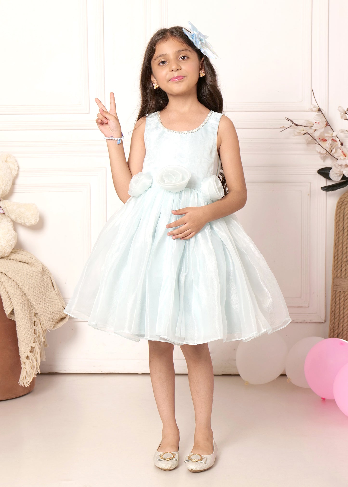 A young girl confidently posing in a floral blue dress, showcasing delicate fabric details and matching shoes, perfect for spring or summer occasions.