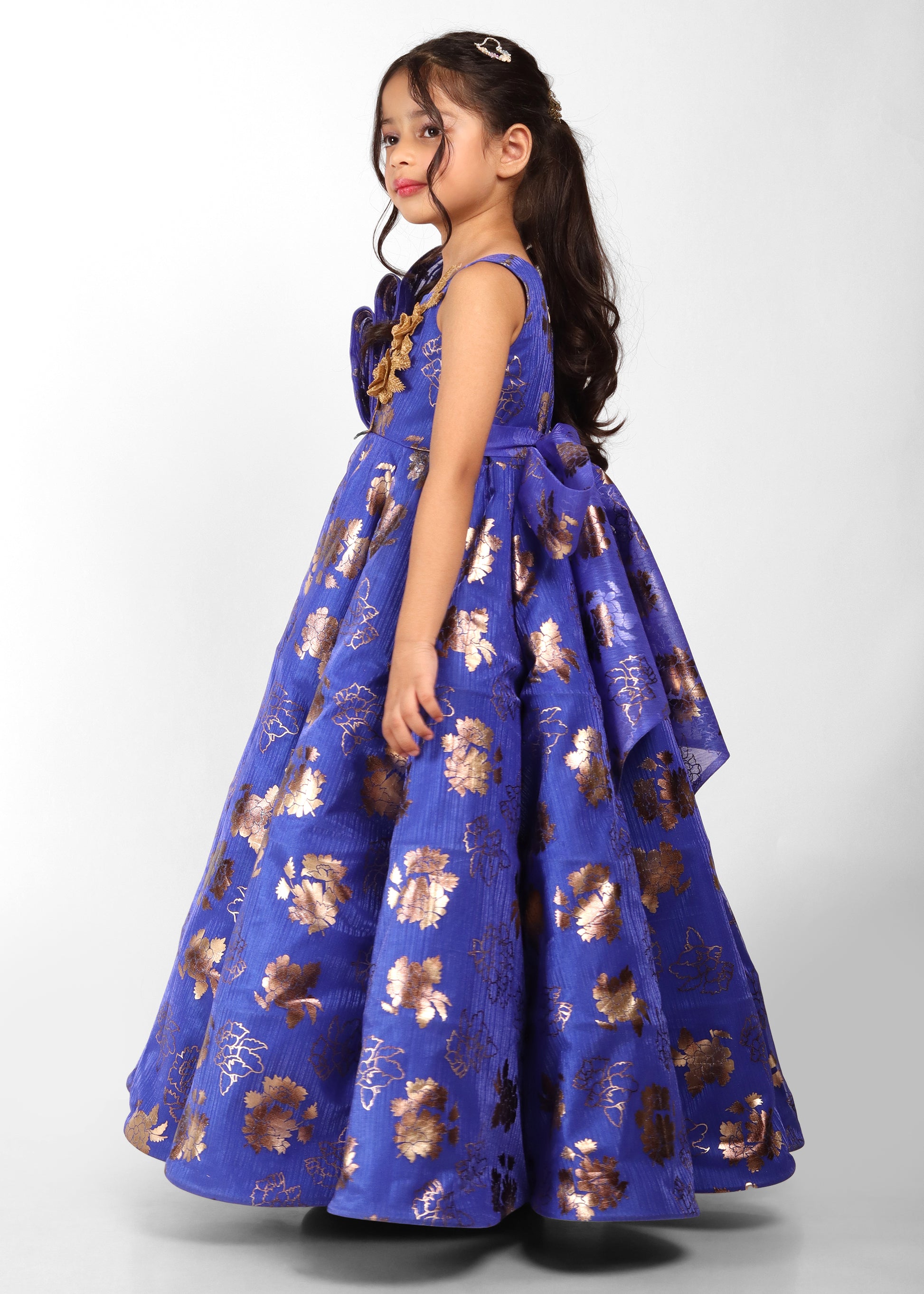 Side view of a girl in a blue floral gown with gold accents, showcasing flowing fabric and elegant style