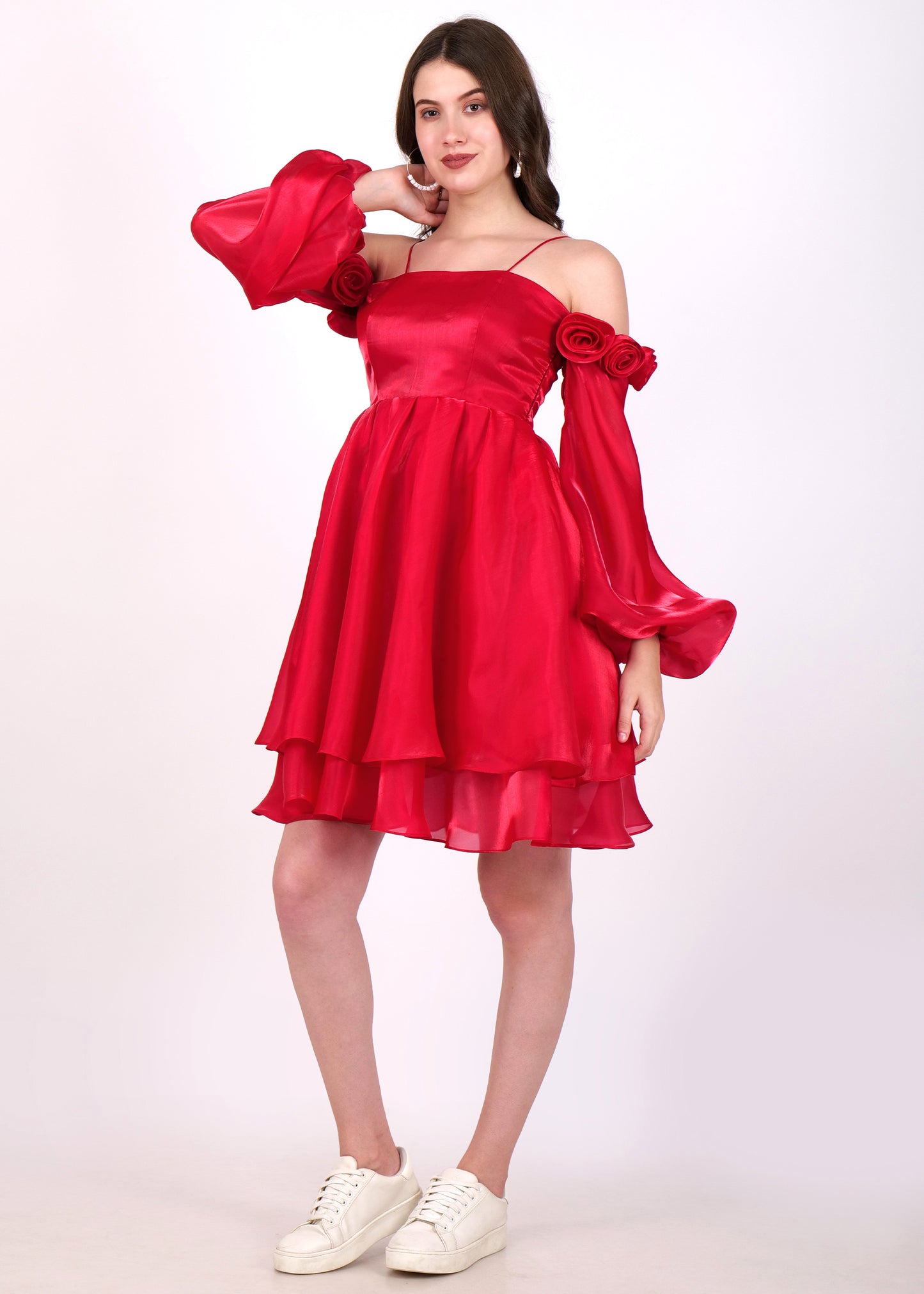 Woman showcasing a side view of a red layered dress with off-shoulder rose sleeve detailing, styled with white sneakers.