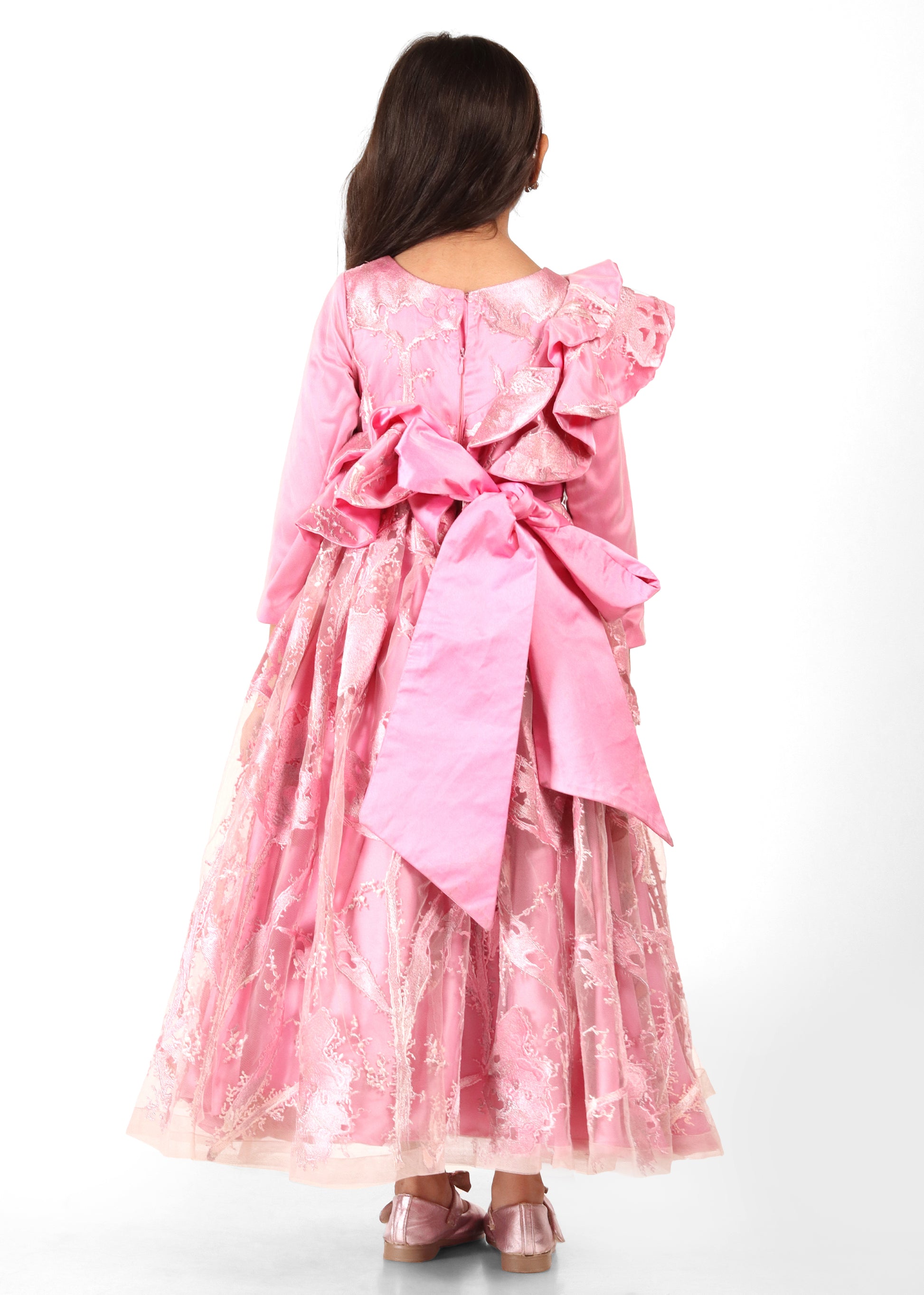 Child in an elegant pink gown with large back bow, showing off the detailed floral lacework on the back.