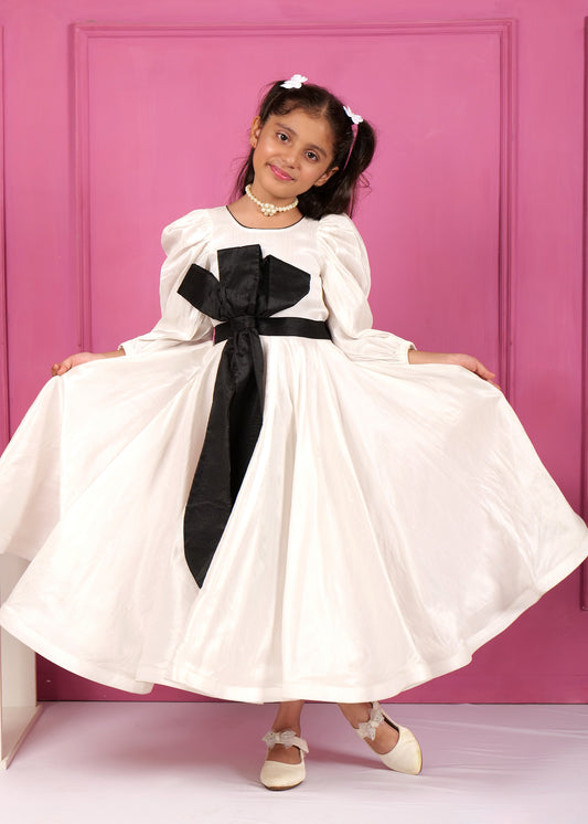 Little girl twirling in a white puff-sleeve dress adorned with a black bow, showcasing the flowing skirt in front of a pink wall