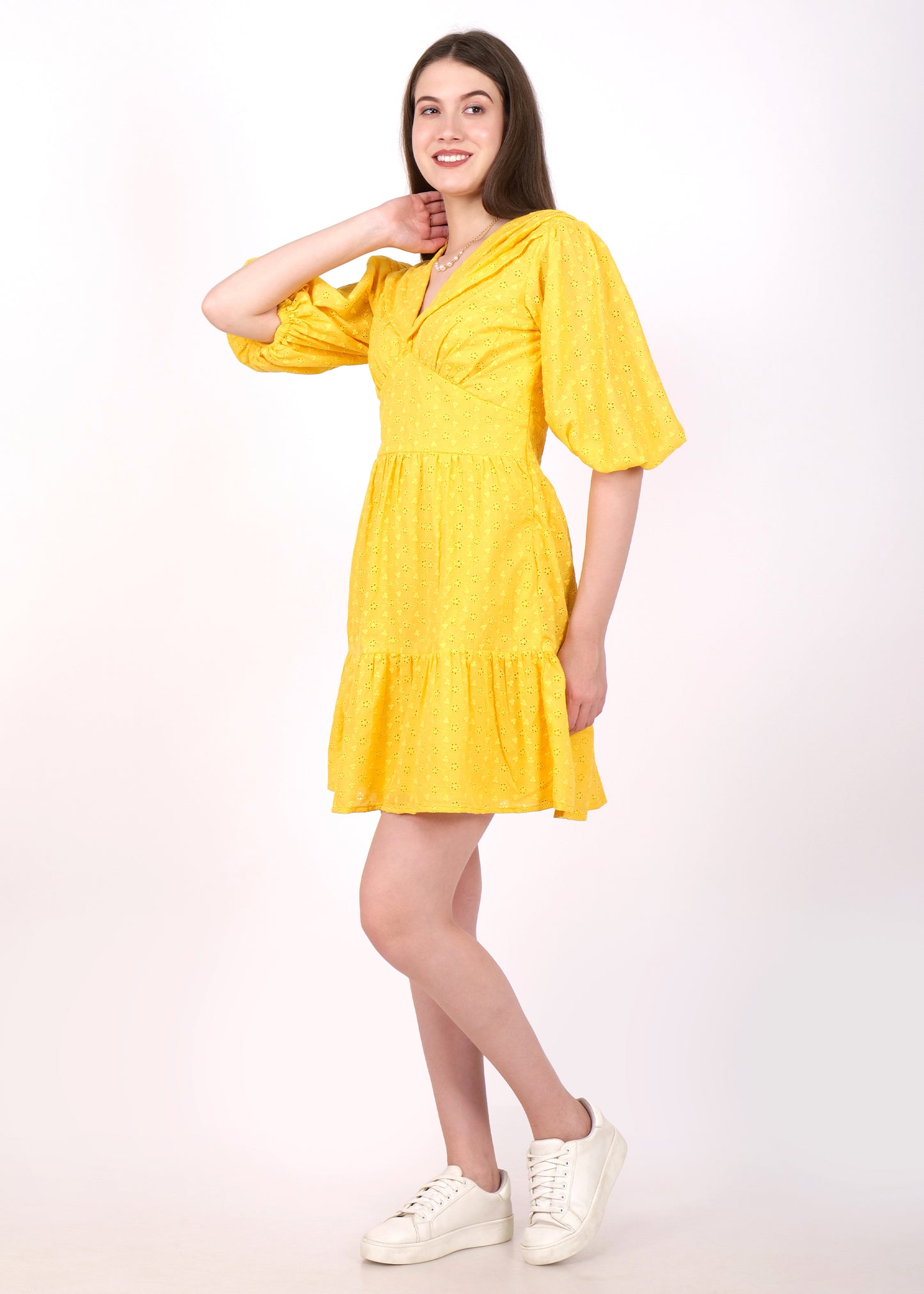 Side view of a woman in a bright yellow puff sleeve dress paired with white sneakers, smiling and posing gracefully