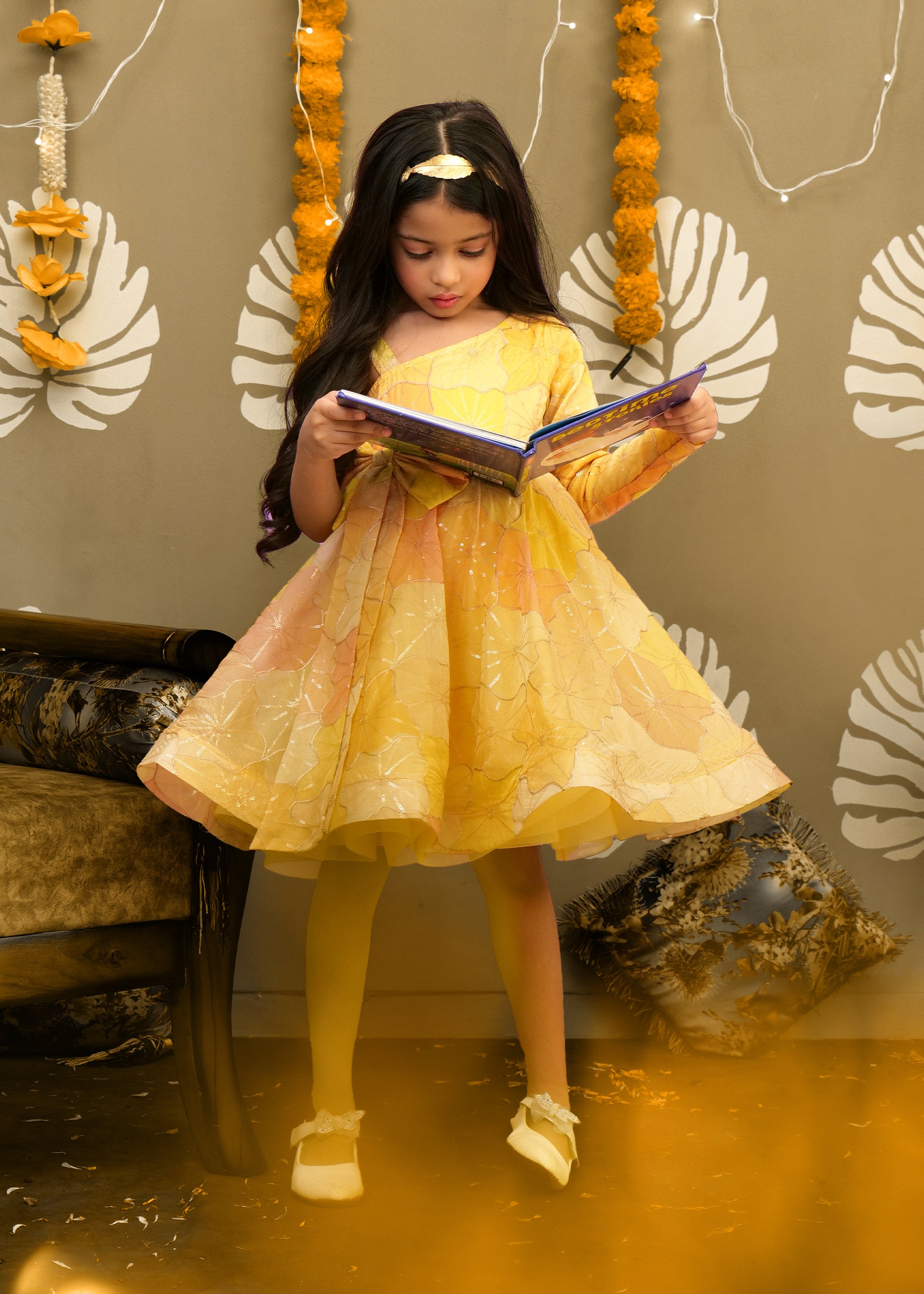 "Charming girl reading a book in a bright yellow one-shoulder dress, designed for special festive celebrations."