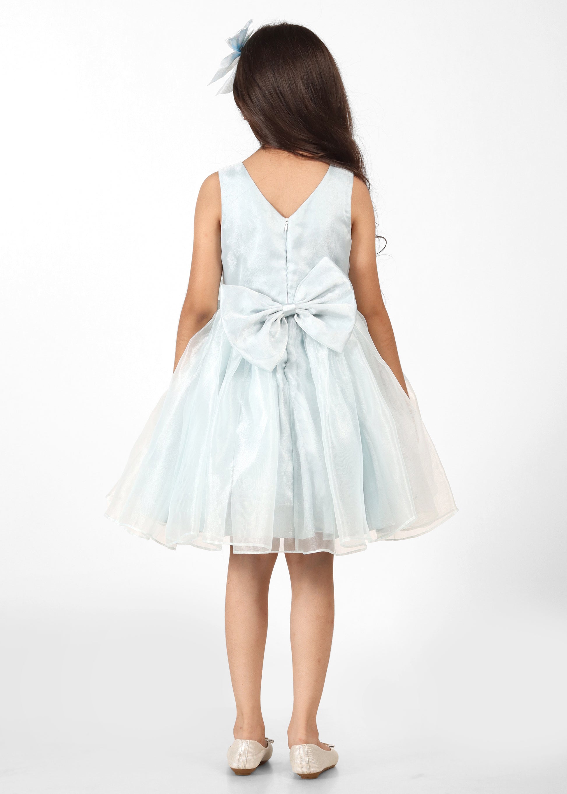 A young girl showing the back of her pastel blue dress, highlighting the intricate bow design and flowing fabric.