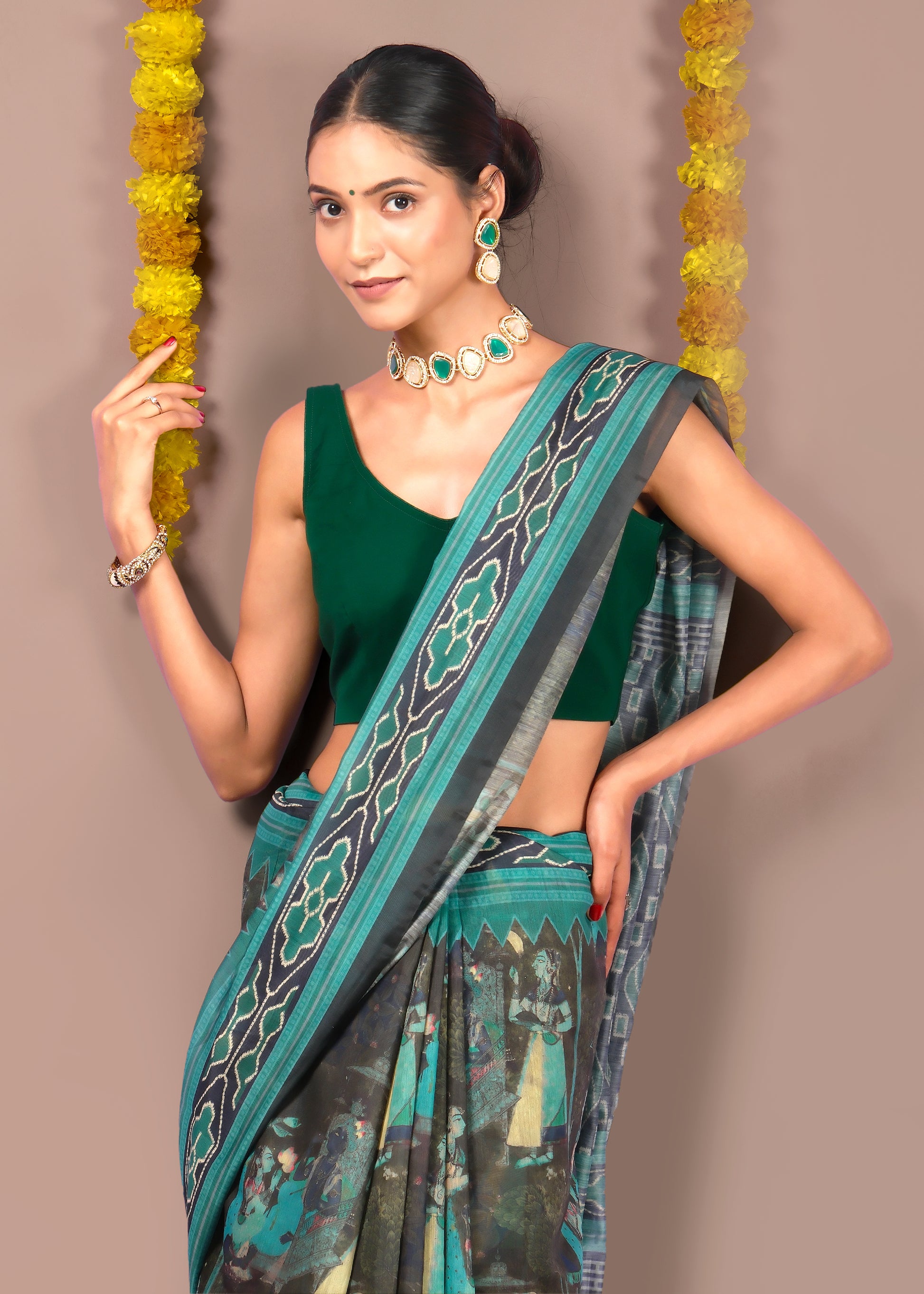 Close-up of a model in a green blouse and green saree with black patterns, showcasing her jewelry and saree's design