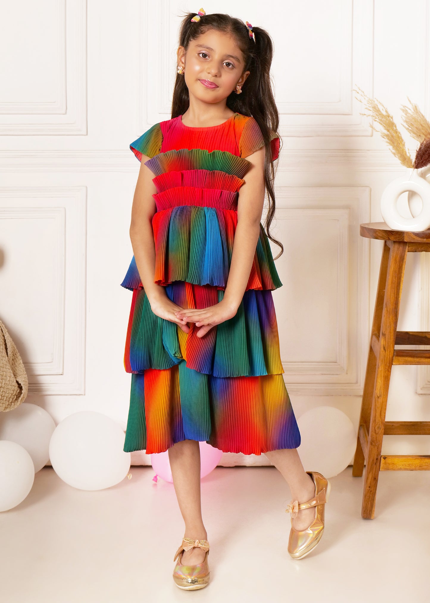 "Girl in colorful pleated dress, standing and smiling, kids party outfit, rainbow dress for girls."
