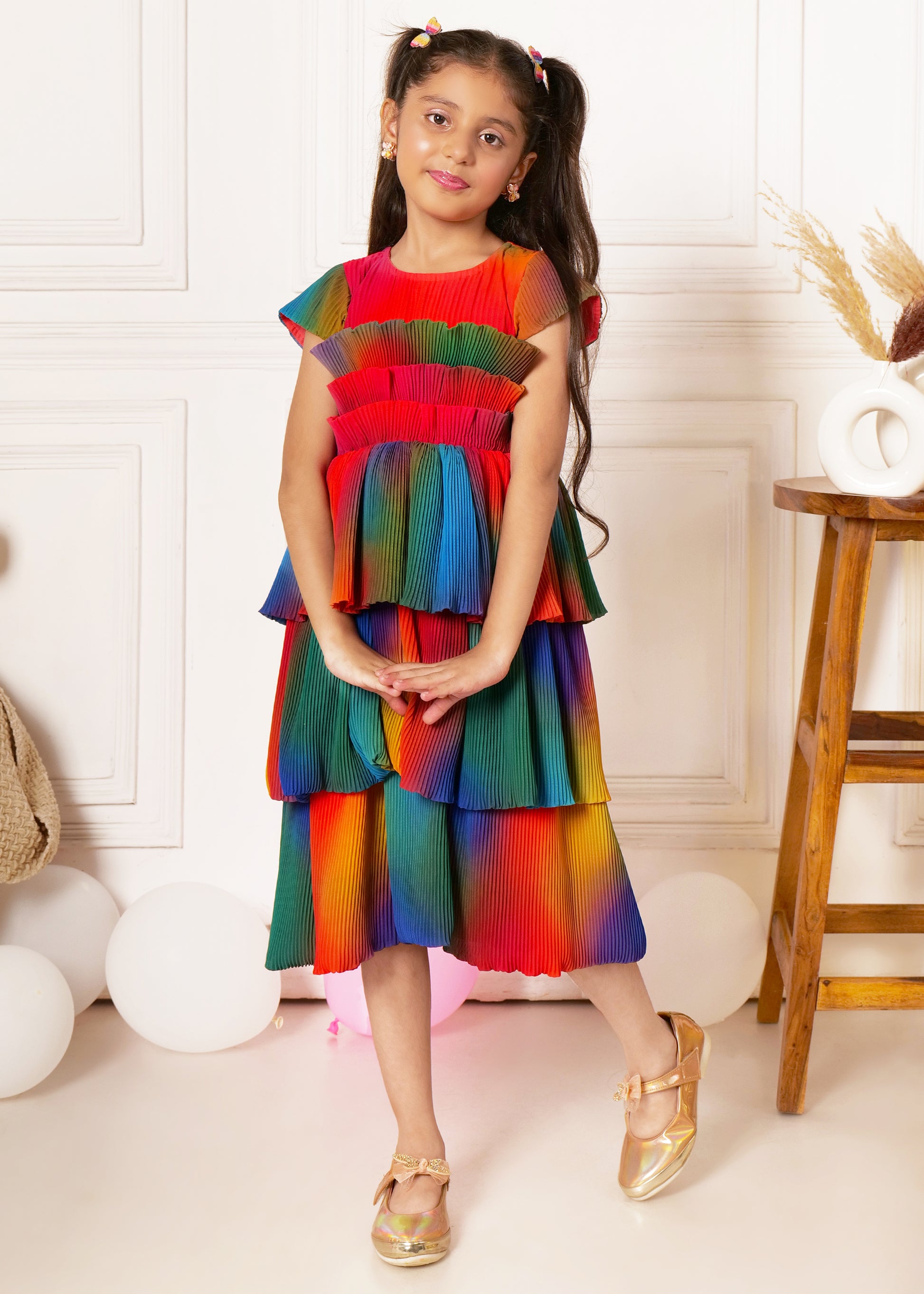 "Girl in colorful pleated dress, standing and smiling, kids party outfit, rainbow dress for girls."