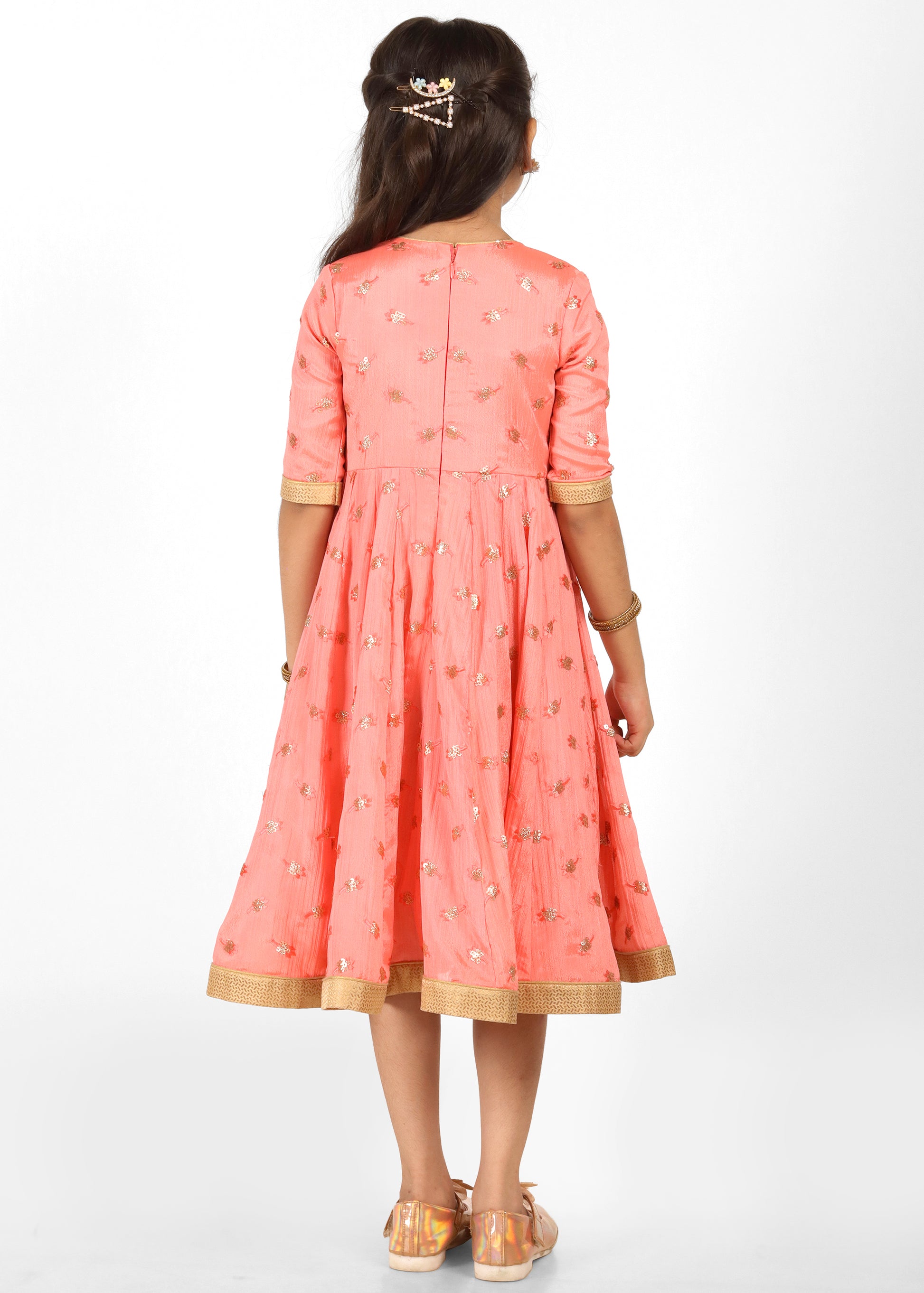 Back view of a peach and gold festive dress with floral embroidery, worn by a young girl posing in a traditional setting.