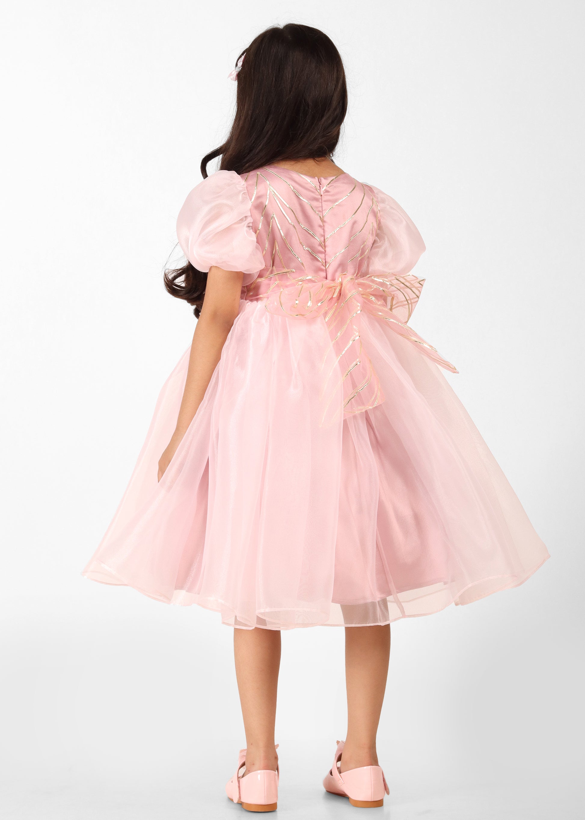 "Back view of a girl wearing a pink organza dress with puff sleeves and a large floral bow, highlighting the beautiful back design."