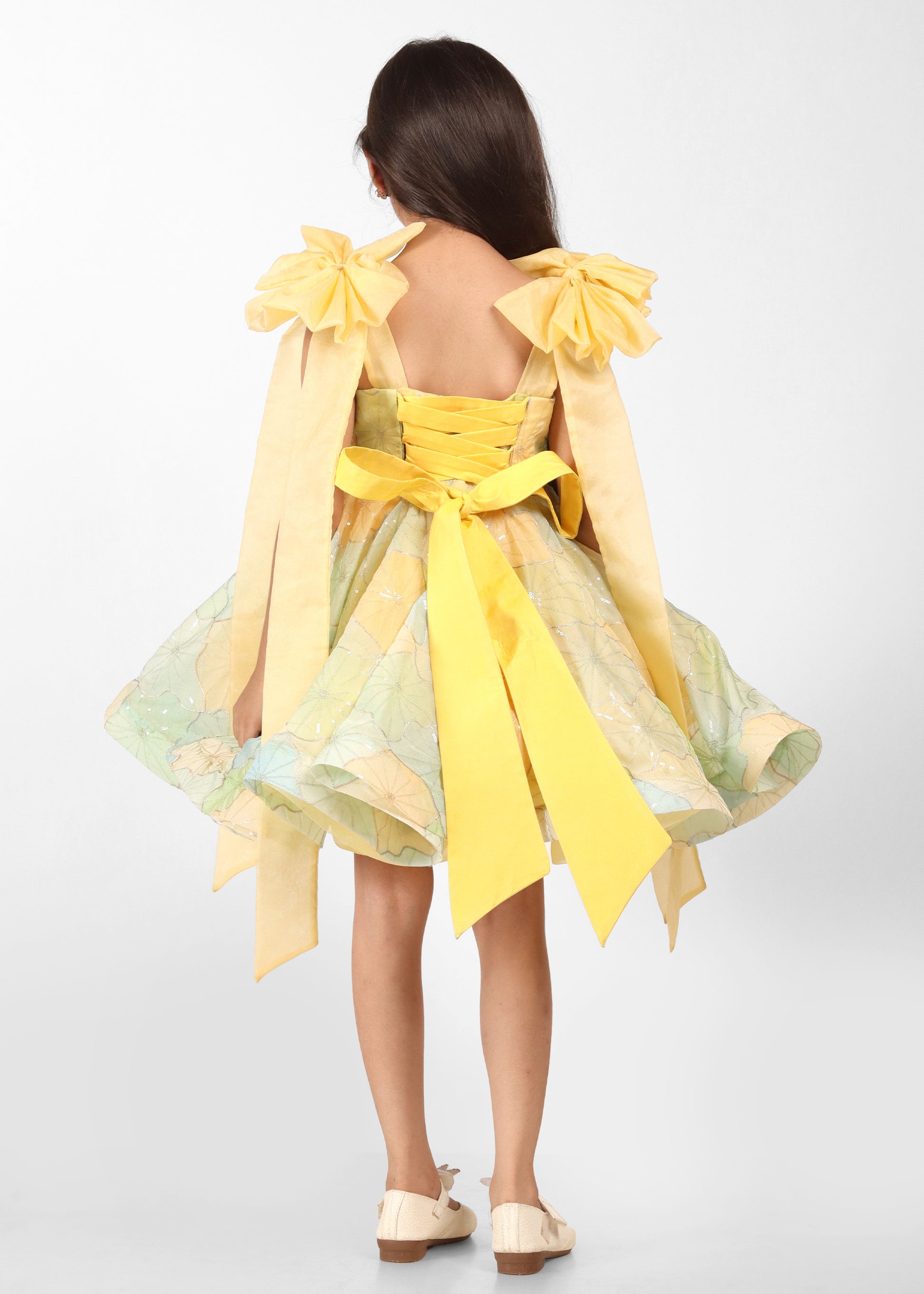 "Back view of a pastel yellow floral dress with large bow accents and a corset-style ribbon tie, adding a touch of grace and sophistication."