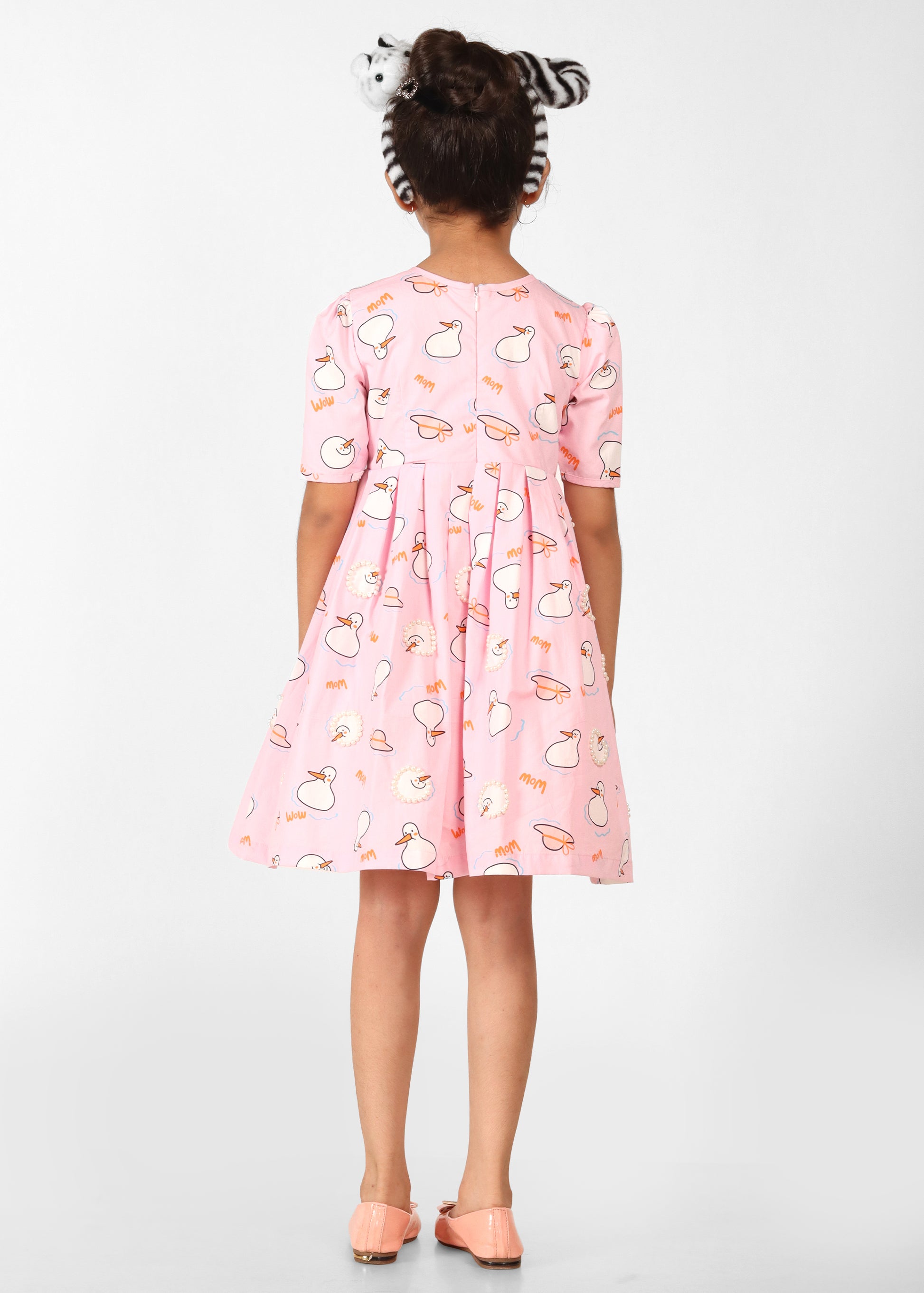 Back view of a girl in a light pink dress featuring playful animal prints, showcasing the dress's comfortable fit and zipper closure