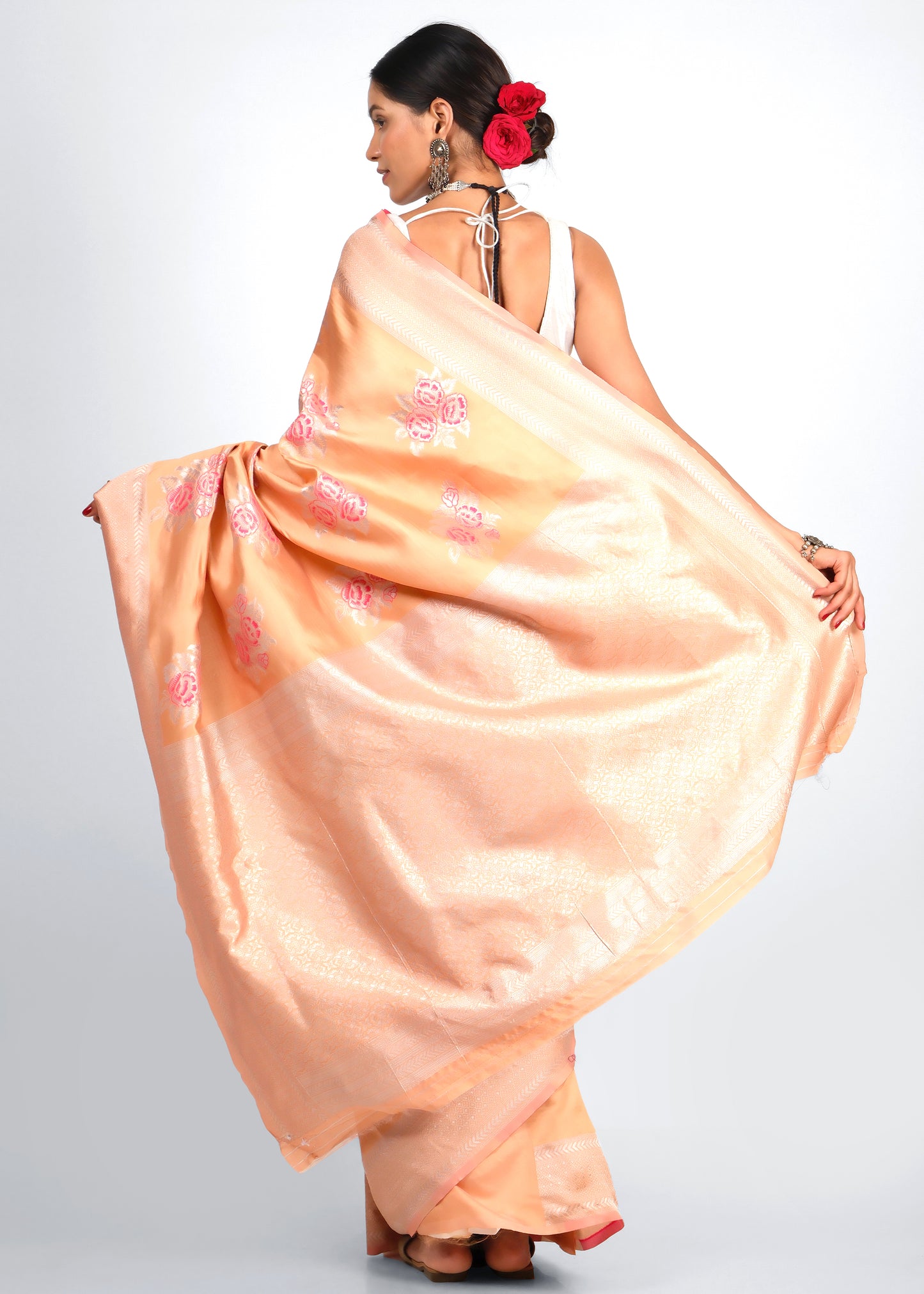 Back view of a peach-colored Banarasi silk saree with silver zari and pink floral motifs, elegantly draped by a model.