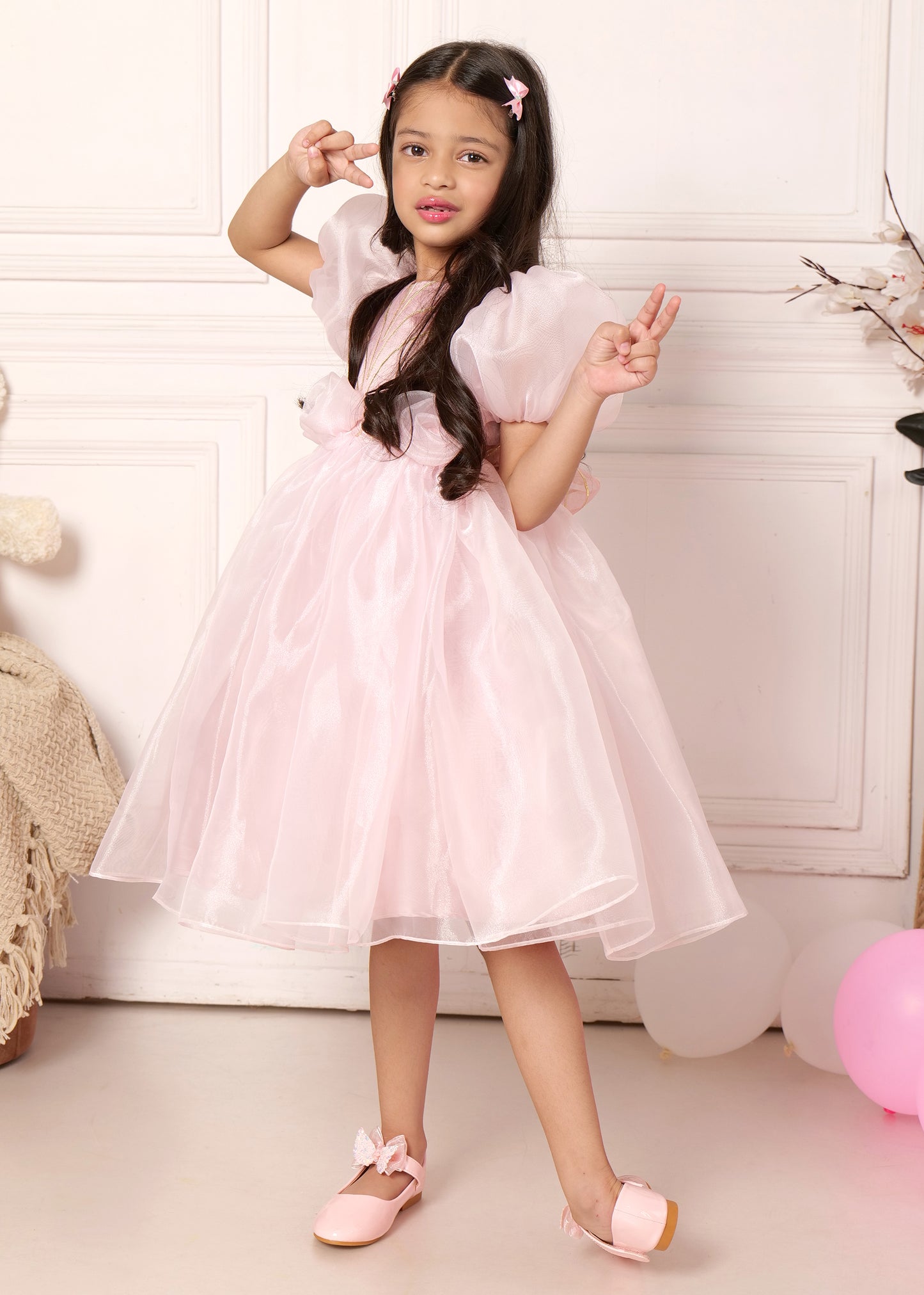 "Adorable girl in a pink party dress with puff sleeves, making a playful peace sign gesture, perfect for birthdays and special occasions."