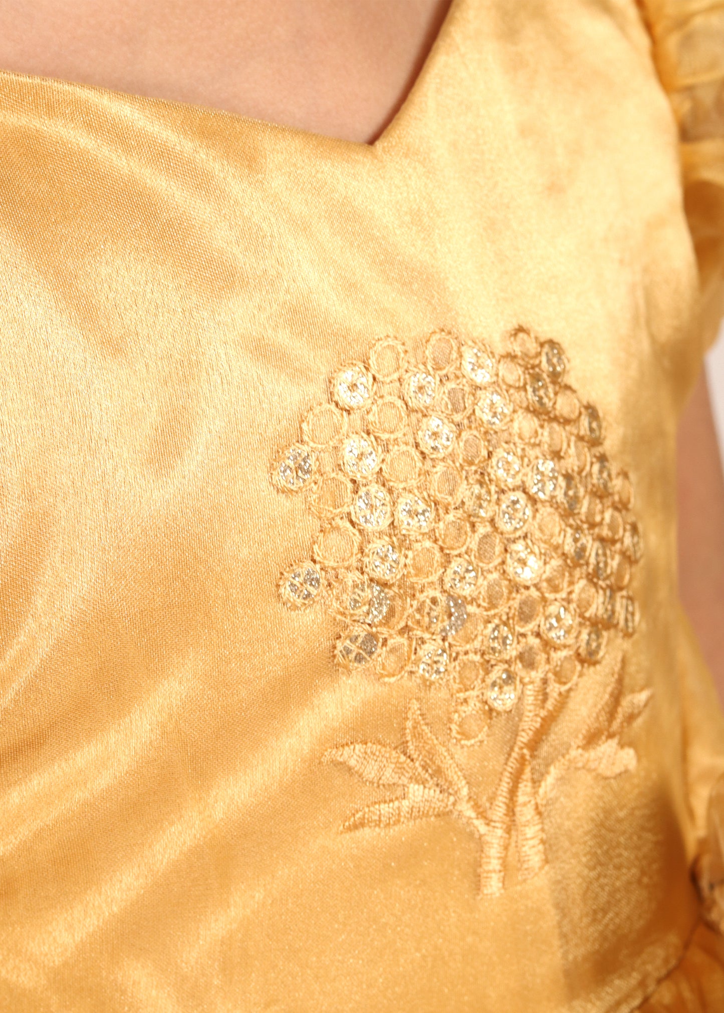 Close-up of gold embroidery on a festive dress, highlighting floral embellishments and detailed craftsmanship.