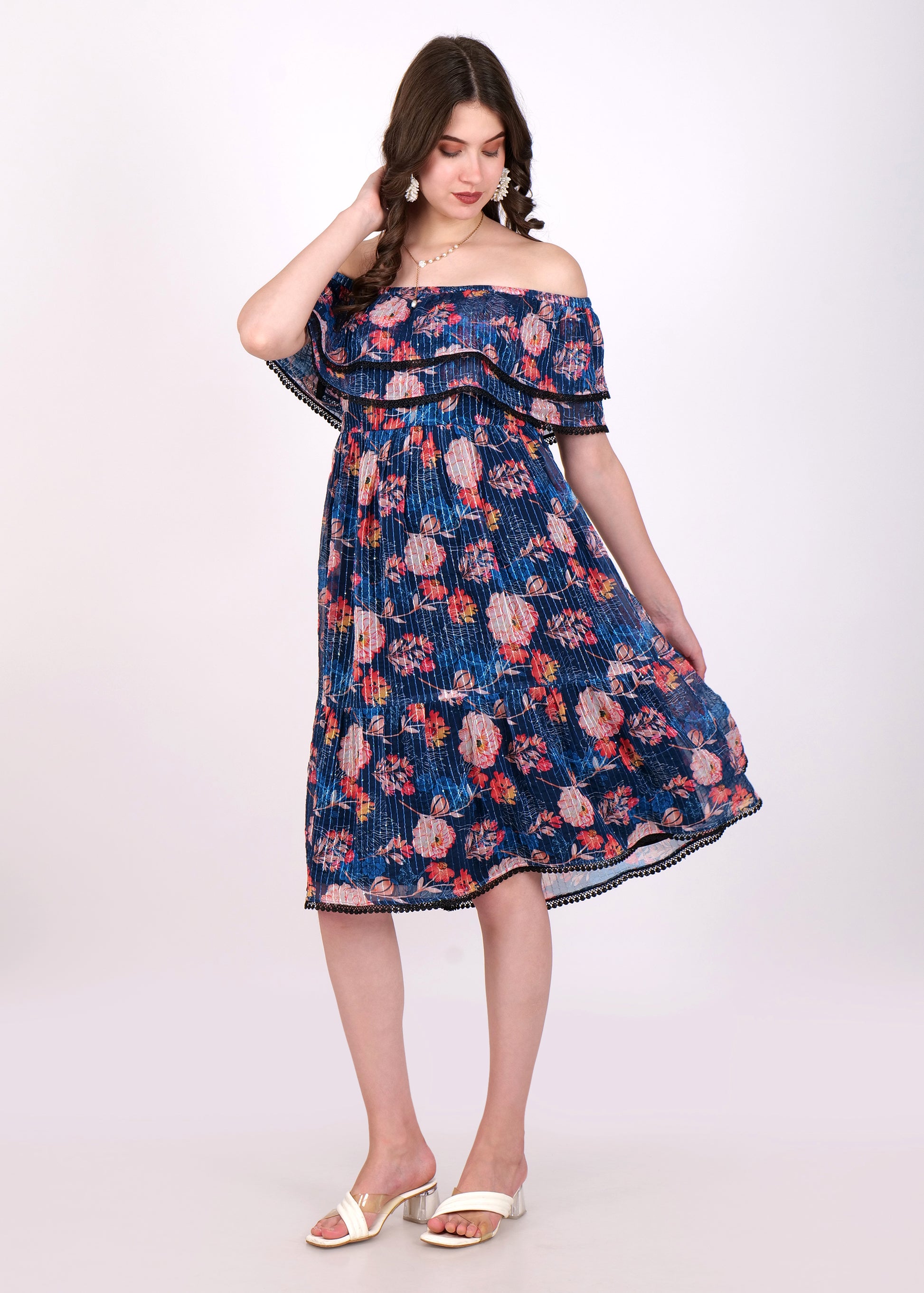 Woman twirling in a navy blue off-shoulder pleated midi dress with floral print and ruffled layers, styled with white sandals