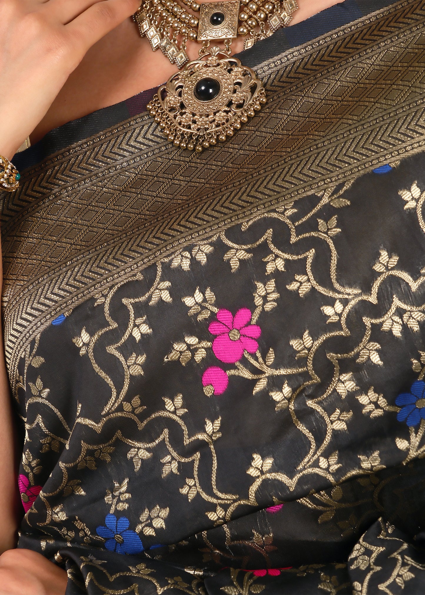 Close-up of black Banarasi saree’s intricate gold zari weave and floral motifs in contrasting pink and blue