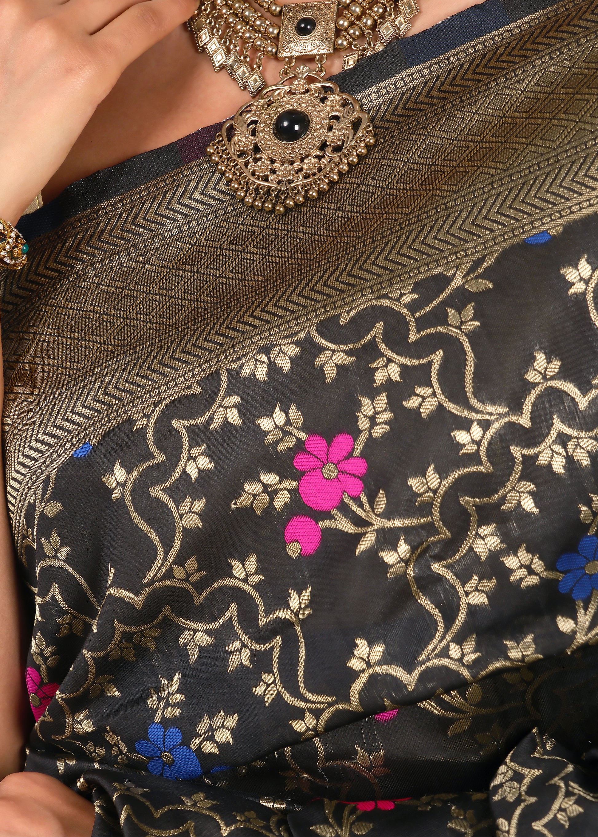 Close-up of black Banarasi saree’s intricate gold zari weave and floral motifs in contrasting pink and blue