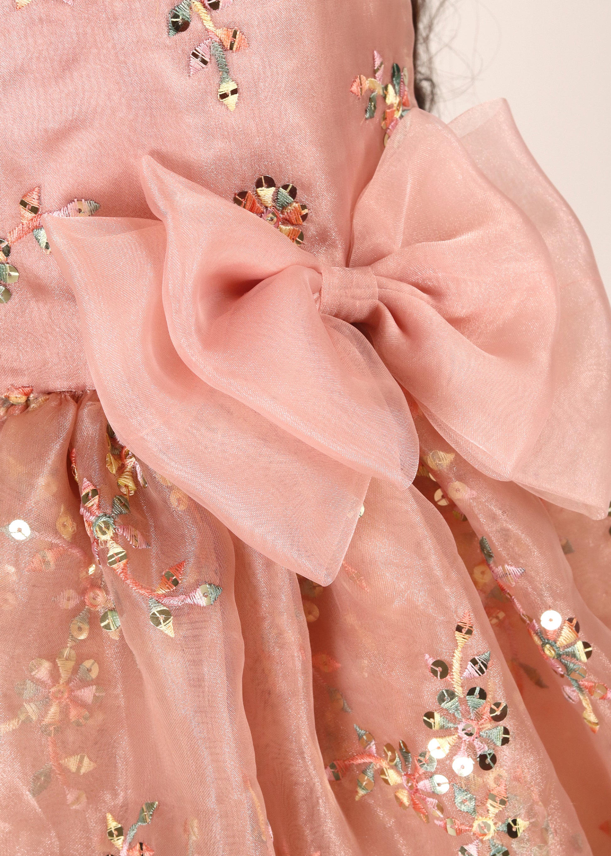 Close-up of the bow and sequin embroidery on a peach floral dress, highlighting the delicate craftsmanship of the design.