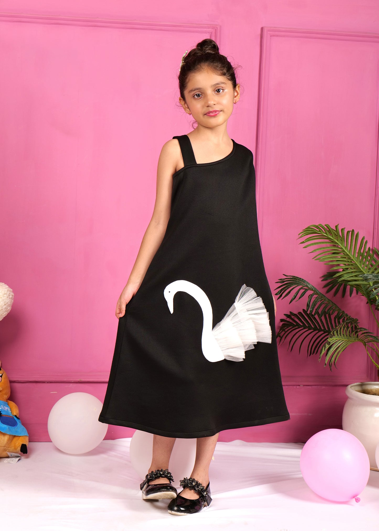 Girl in a black asymmetrical dress with white swan applique posing confidently against a pink background