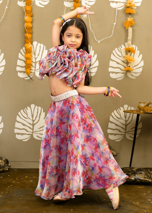 Little girl performing a dance pose in a vibrant lehenga and ruffle blouse, set against a traditional festive backdrop.