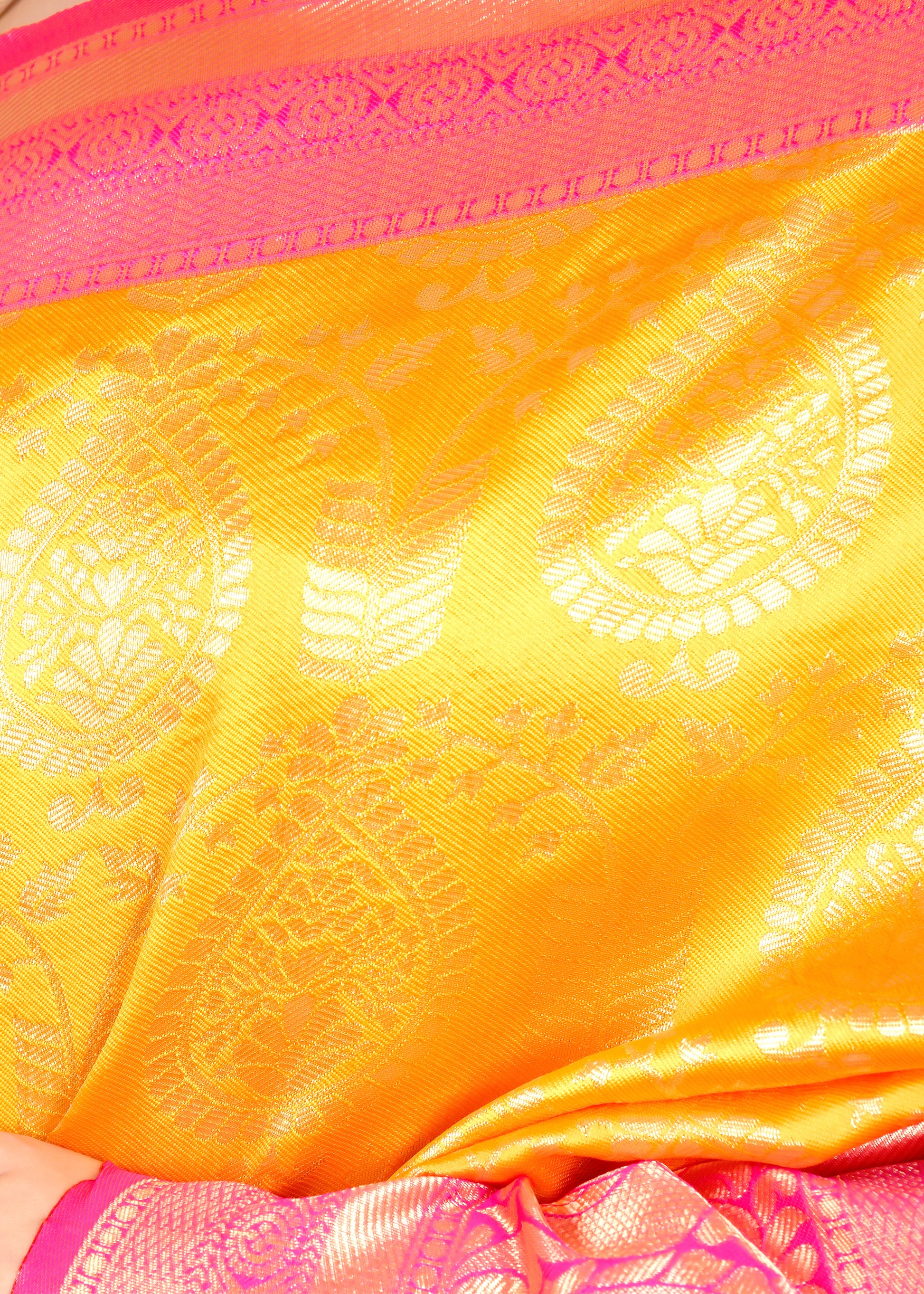 Close-up of an orange silk saree with golden woven motifs and a bright pink border, showcasing fine craftsmanship and rich texture