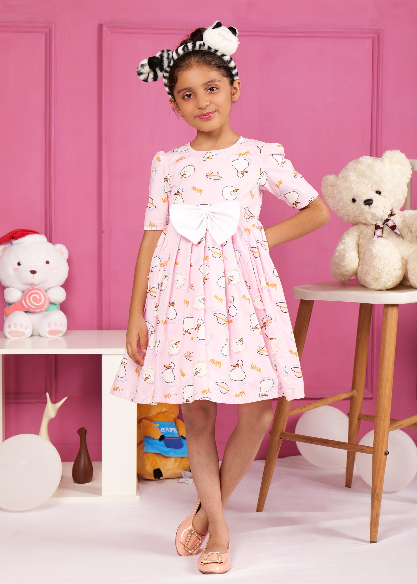 Adorable girl modeling a pink swan-themed dress with puffed sleeves, styled with a black and white headband, perfect for a fun day out